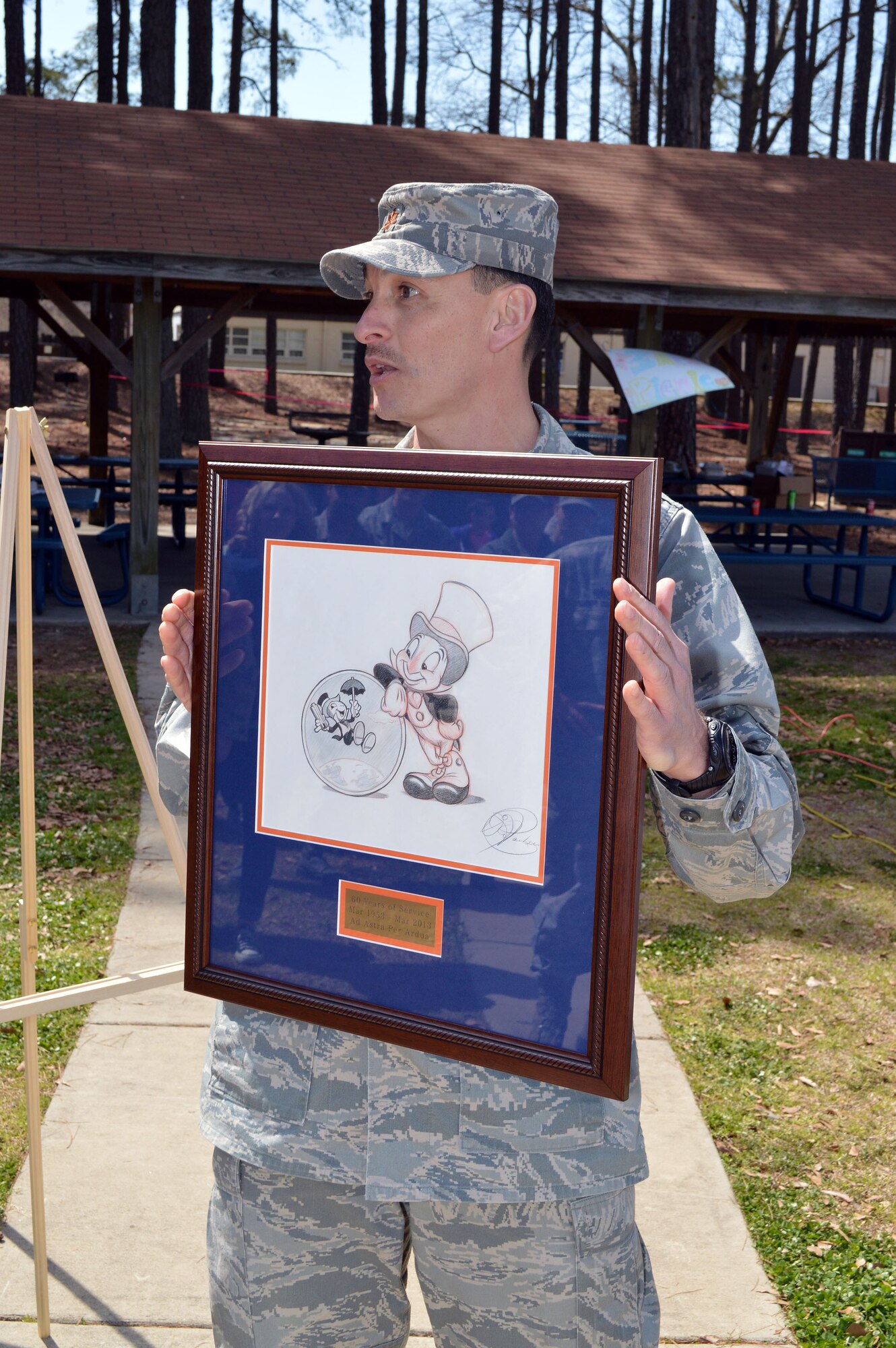 Maj. Joseph Whittington, 3rd Aerial Port Squadron commander, unveils an original Disney caricature drawing of the squadron's mascot, Jiminy Cricket, during a picnic March 29, celebrating the squadron's 60th Anniversary at Pope Army Airfield, Fort Bragg, N.C.
