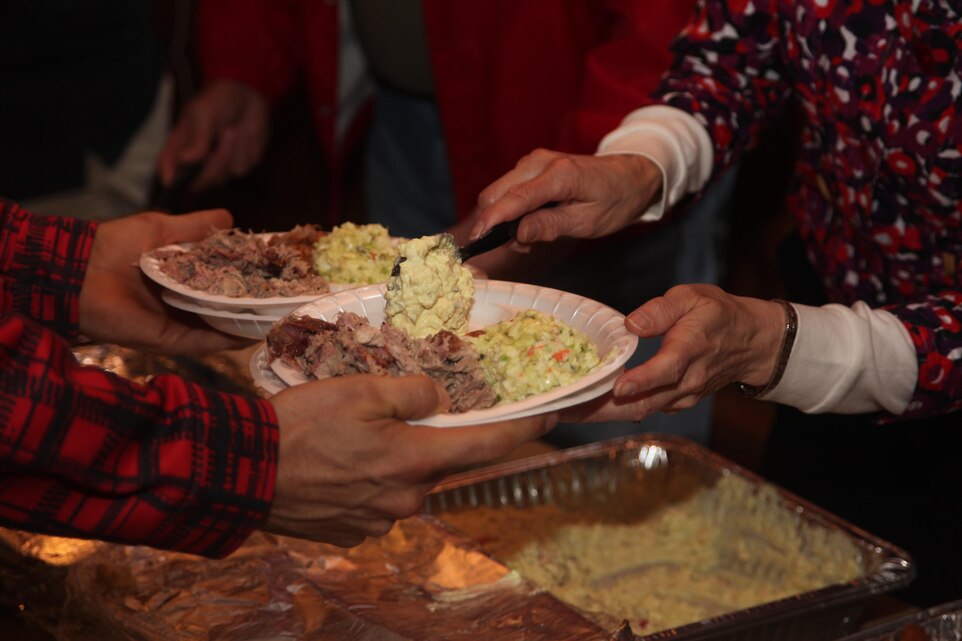 A Marine holds his plate as a Havelock Military Affairs Committee member serves him potato salad as a part of a free meal during the Havelock MAC Pig Pickin at Hancock Marina March 27. More than 200 Marines, Sailors and family members attended the event and enjoyed an Easter Carolina treat. “A Pig Pickin is a local tradition and a lot of these families are not from around here,” said Stephanie Duncan, the executive director of the Havelock Chamber of Commerce. “If nothing else, I hope they leave here with full stomachs and just a bit more relaxed then when they came in.”