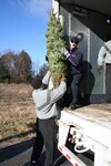 Staff Sgt. Daniel Branner, a New York Army National Guard Citizen-Soldier with the 42nd Infantry Division, passes a donated Christmas tree to FedEx driver Don Pelletier at Ellms Farms in Charlton, N.Y., Nov. 28. The trees are part of a donated shipment for DoD installations in the United States and across the globe as part of the "Trees for Troops" charitable donations for 2007. Brunner volunteered his time to help other area veterans and military family members in loading more than 150 trees for shipment.
