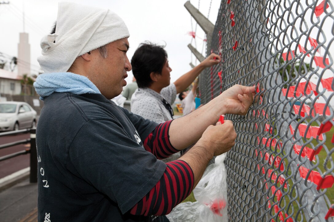 Masamichi Sakihama untangles ribbon from the fence March 24 at gate 3 on Marine Corps Air Station Futenma. Okinawa citizens, Marines and status of forces agreement personnel volunteer to clean the fences weekly to help keep Ginowan City clean. “We clean the fences because we want to make this the nicest place in Ginowan City,” said Sakihama, a volunteer with the Okinawa Osprey fan club.