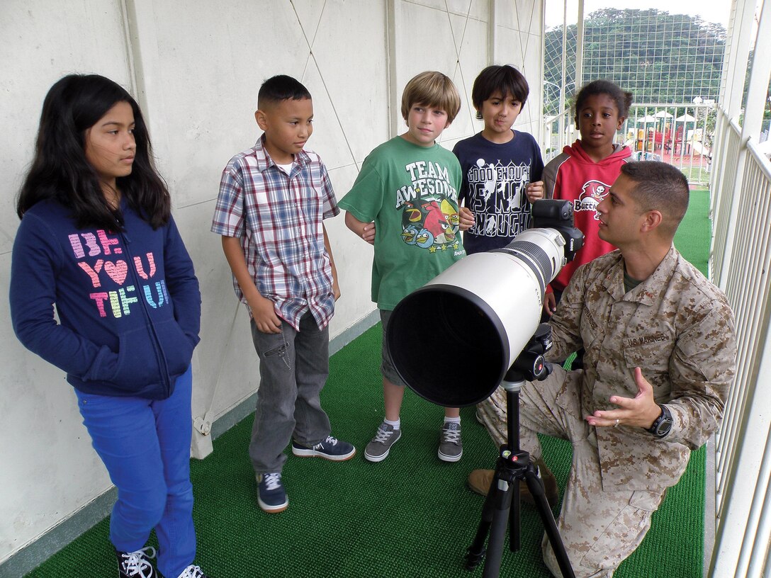 Chief Warrant Officer Georgi Hernandez shows students how to use a camera and zoom lens March 29 during a career day at E.C. Killin Elementary School. More than 40 active-duty and civilian volunteers presented main aspects of their professions to students throughout the day, including orthopedic surgery, photography, accounting and emergency services. Hernandez is a combat camera officer and deputy director of the Consolidated Combat Camera Center on Camp Foster. 