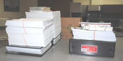 On the left are two piles of publications issued to students. After the 12th Operations Support Squadron went digital, the small pile of publications on the right is all that is required for students. (U.S. Air Force Photo by Capt. Ashley Walker)