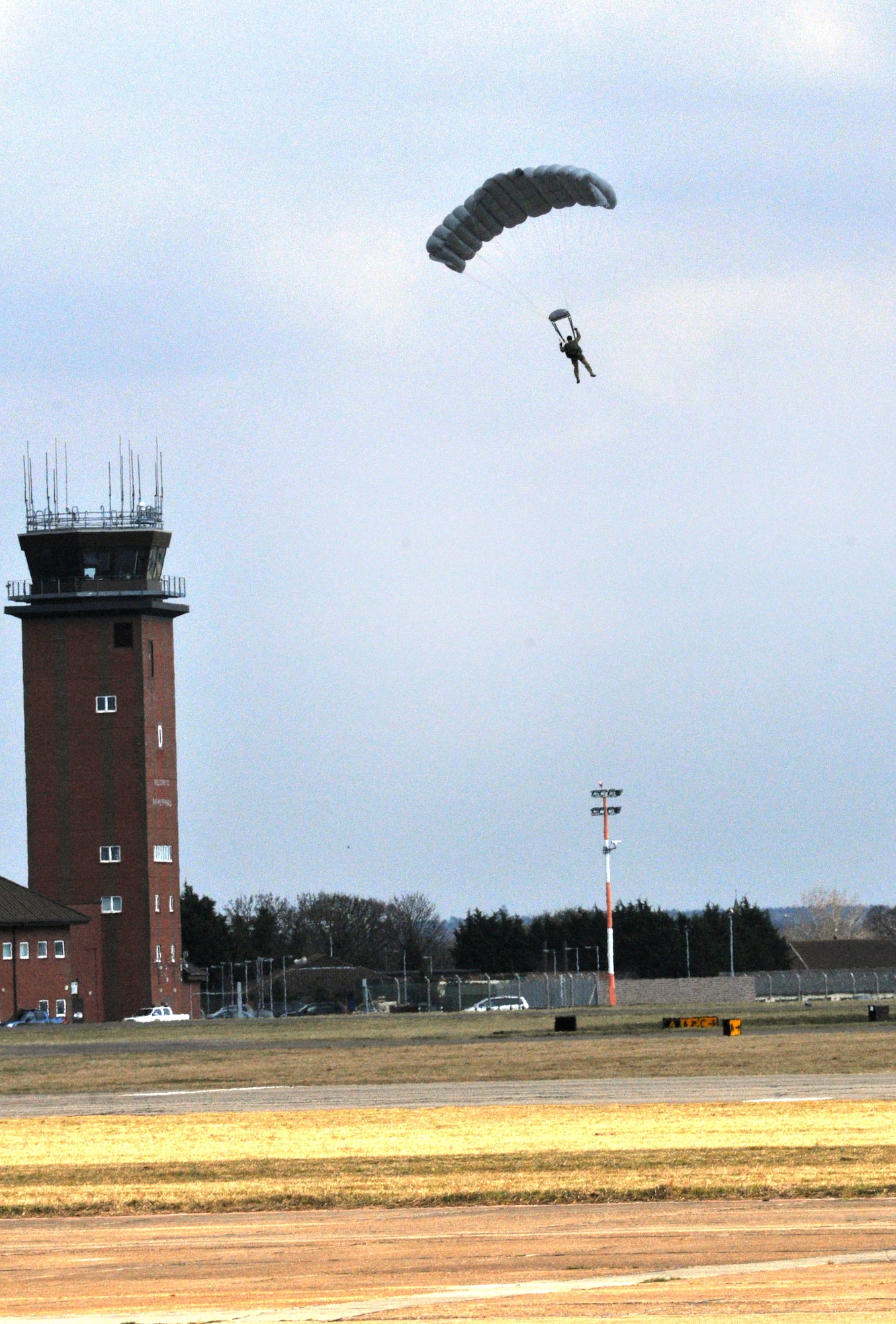 An Airman from the 321st Special Tactics Squadron freefalls past the base air traffic control tower during a demonstration March 28, 2013, near hangar 539 on RAF Mildenhall, England. The freefall demonstration was part of the 352nd Special Operations Group Heritage Week. (U.S. Air Force photo by Airman 1st Class Kelsey Waters/Released)