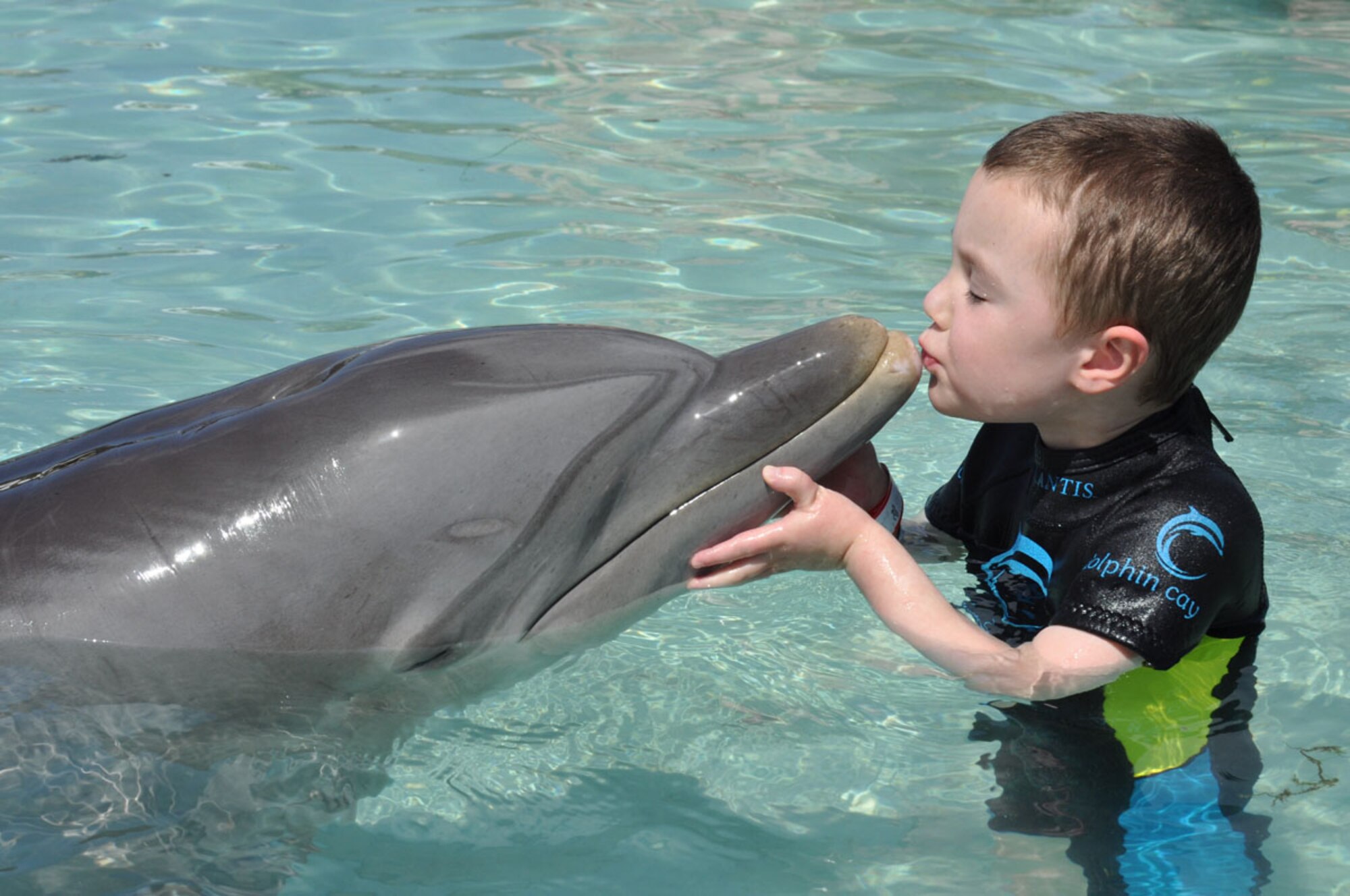HANSCOM AIR FORCE BASE, Mass. – Parrish Auzenne kisses a dolphin during his trip to the Atlantis Resort, Bahamas, where the Make-a-Wish Foundation sent him, along with his family, to experience his dream of swimming with the dolphins. Auzenne was born with a life-threatening congenital heart defect called Hypoplastic Left Heart Syndrome that required him to have three open heart surgeries by age three. (Courtesy photo)