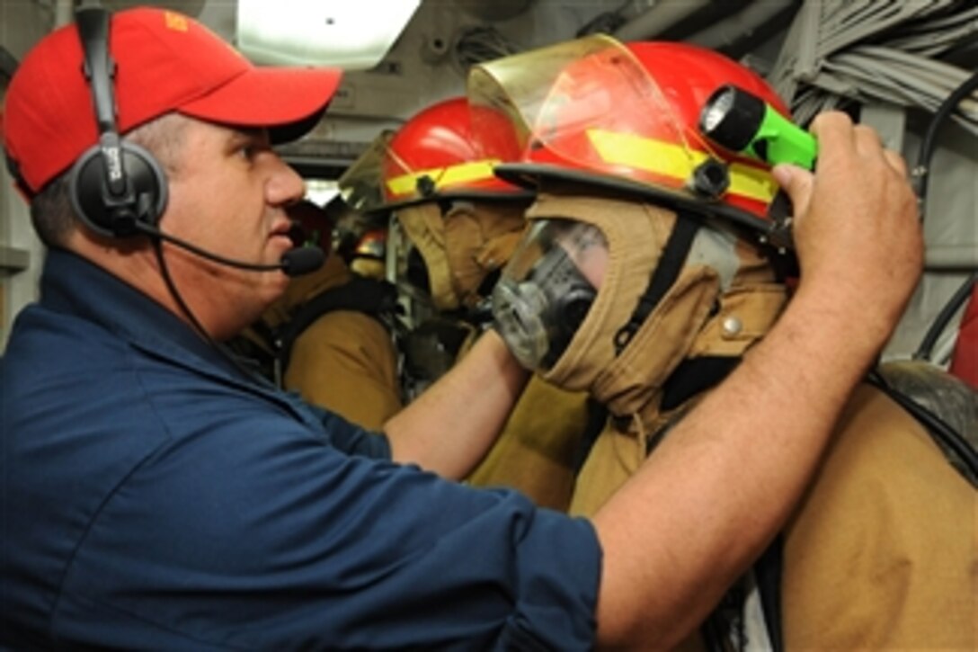 Chief Petty Officer Thomas Butler, left, adjusts a sailor’s firefighting helmet during a fire drill aboard the guided-missile cruiser USS Hue City (CG 66) as the ship operates at sea on April 2, 2013.  The Hue City is deployed to the 5th Fleet area of responsibility to conduct maritime security operations and theater security cooperation efforts.  
