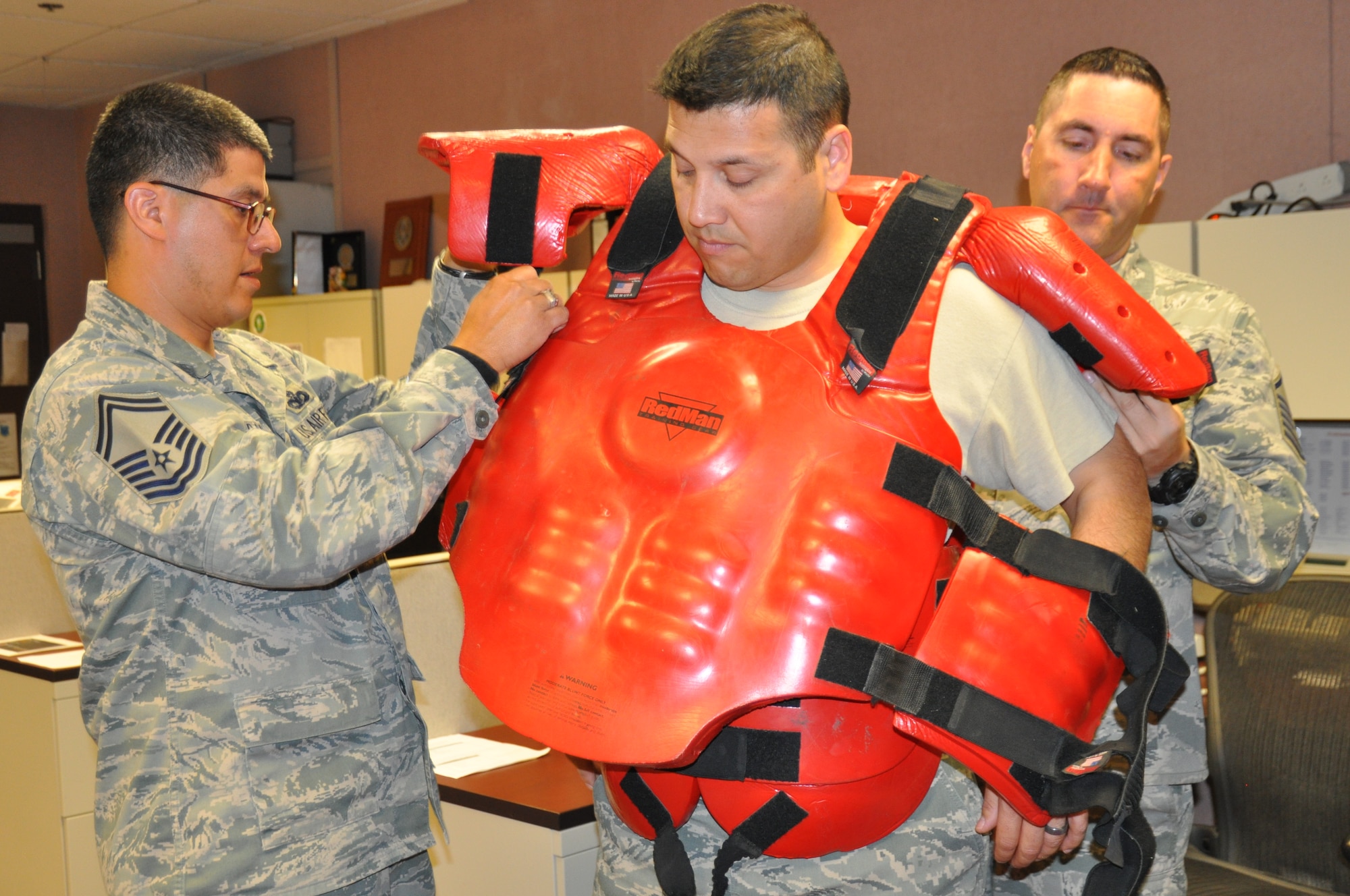 Senior Master Sgt. Benjamin Miranda and Master Sgt. Robert Danylchuk, 12th Air Force (Air Forces Southern) Force Protection, assist Master Sgt. Paul Azevedo, 12th AF (AFSOUTH) A4/7, in putting on the “red-man” suit in preparation for an organizational active-shooter exercise at Davis-Monthan AFB, Ariz., April 4. (USAF photo by Master Sgt. Kelly Ogden/Released). 