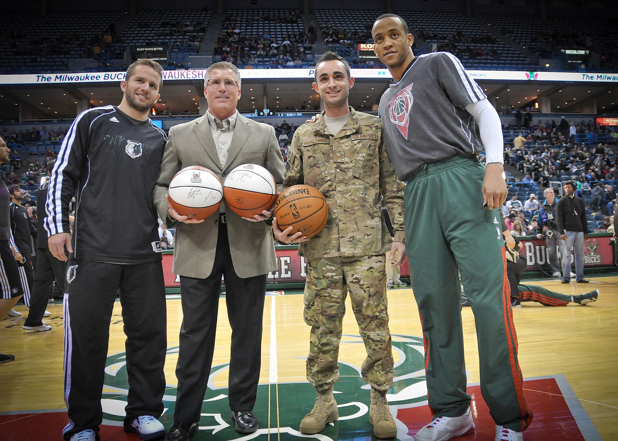 Senior Airman Jefferson Harkleroad poses for photographers with Minnesota Timberwolves team captain Jose Barea, Michael Steger of Waukesha Metal Products and Milwaukee Bucks team captain Monta Ellis at center court of the BMO Harris Bradley Center in Milwaukee Wed., April 3, 2013. (Air National Guard Photo by 1st Lt. Nathan Wallin / Released)
