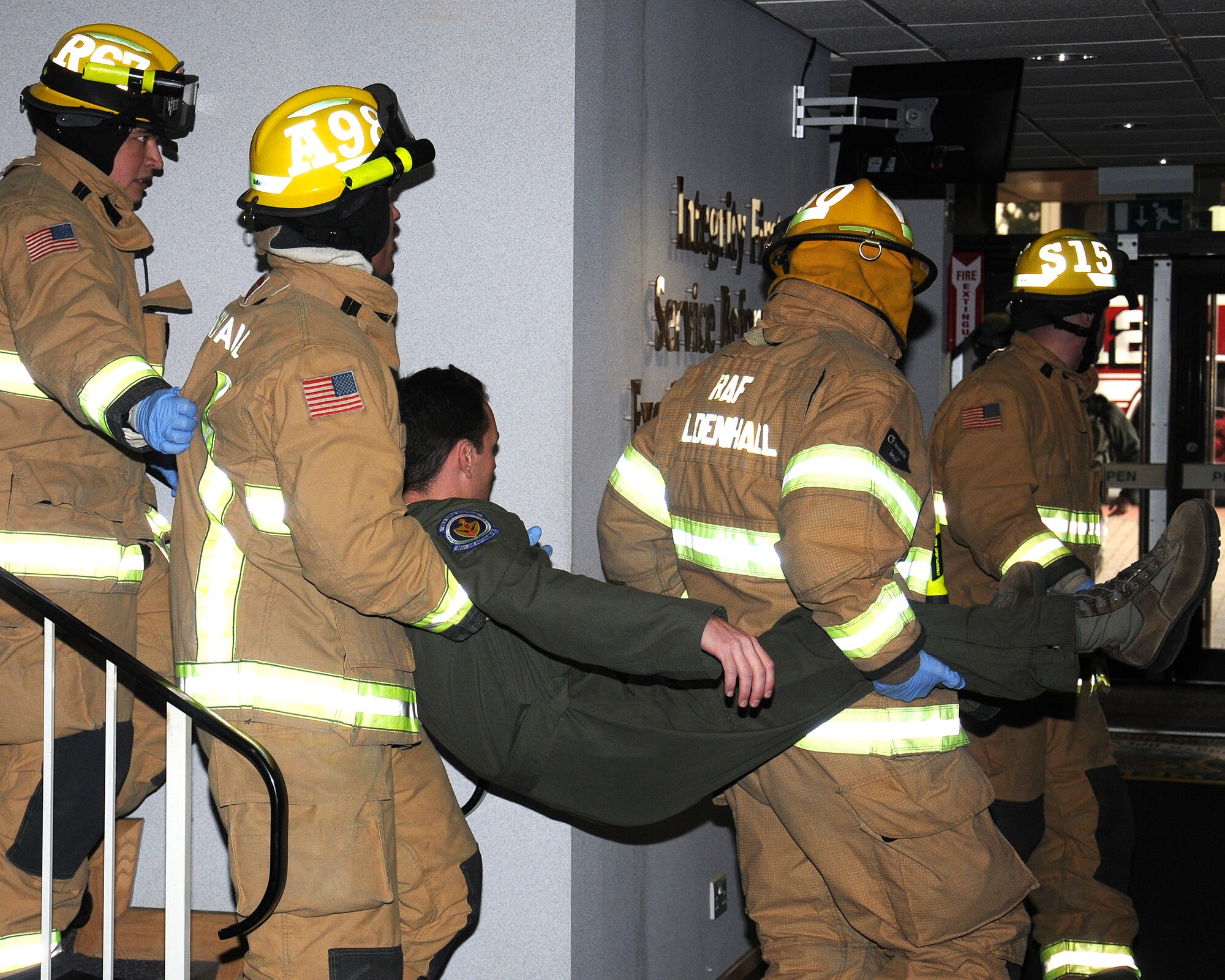 Firefighters from the 100th Civil Engineer Squadron Fire Department move a simulated patient to an ambulance for medical care during an exercise March 28, 2013, at RAF Mildenhall, England. The firefighters utilized a two-man carry to transport a simulated-injured Airman to the casualty collection point where the triage officer, also a firefighter, could determine injury extent and patient transport priority. They also provided additional medical care to injured personnel at the CCP. (U.S. Air Force photo by Gina Randall/Released)