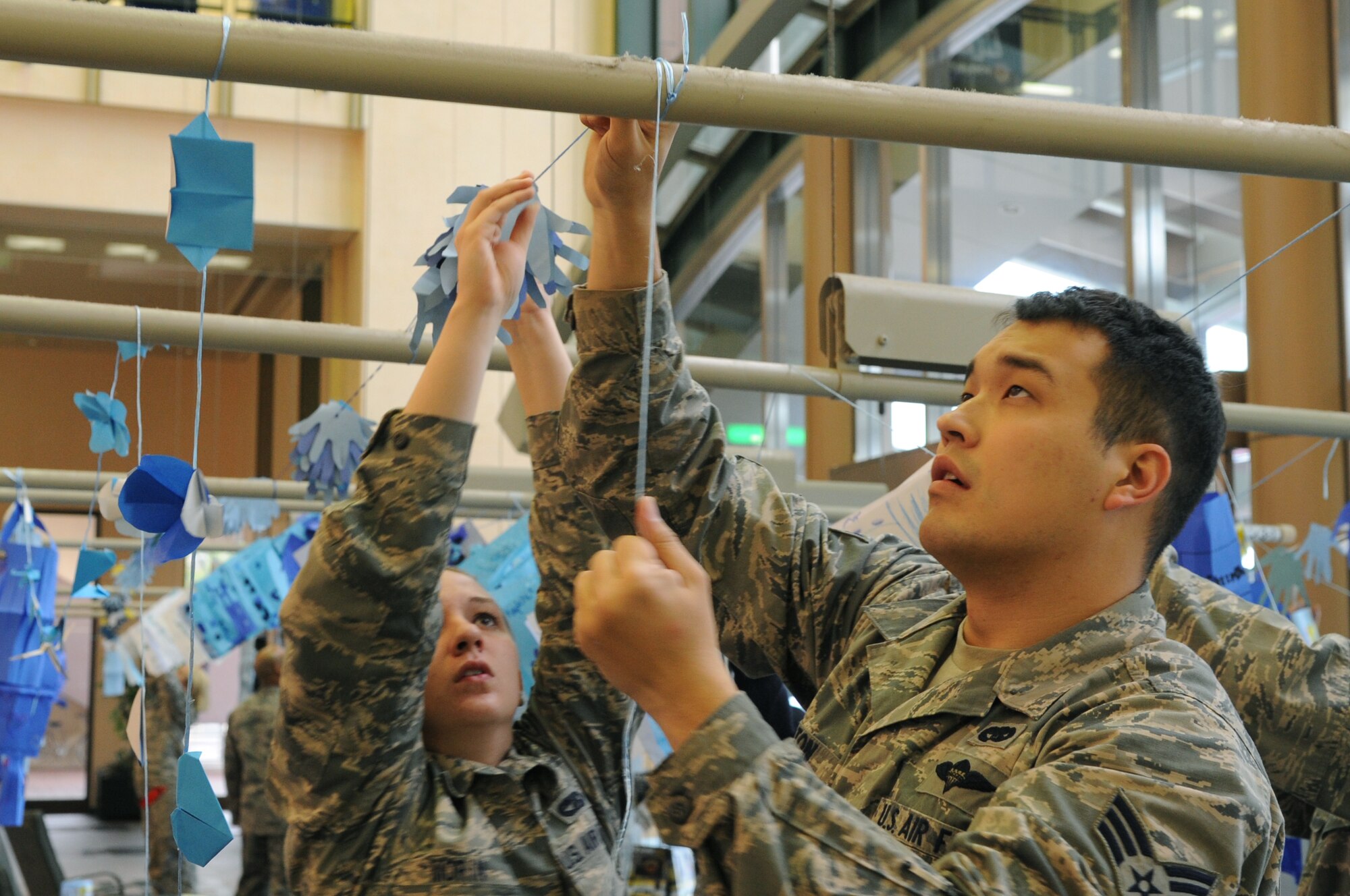 YOKOTA AIR BASE, Japan -- Airman 1st Class Lyndsey Morin and Senior Airman Adam Caton, both from the 374th Logistics Readiness Squadron, hang decorations in support of autism awareness at the Yokota Community Center on Yokota Air Base, Japan, April 2, 2013. The paper decorations were all handmade by Yokota’s elementary, middle and high school students. (U.S. Air Force photo by Airman 1st Class Desiree Economides)