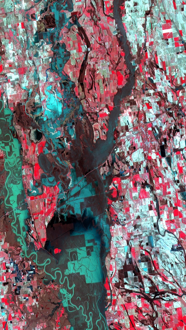 An Eagle Vision satellite image shows a flooded area in Clarendon, Ark., with the original river path in the lower left corner. Farmland appears as red boxes, while darker red shows partially submerged farmland. Green boxes detail property completely submerged by water. Much of the lower middle of this photo shows submerged farmland.