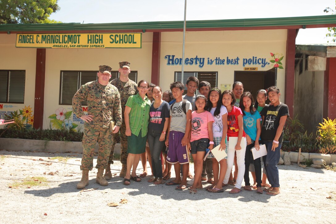 Staff Sgt. Gary Burnett and Lance Cpl. Austin Schey take a picture with the principal and children from Angel C. Manglicmot high school, Angeles, San Antonio, Zambales, Philippines. During Balikatan 2013, Philippine and U.S. service members will conduct humanitarian civic assistance projects throughout Zambales. Preliminary work on community infrastructure projects will begin mid-March. Military medical personnel will offer free medical, dental and veterinary care. Military engineers will construct and repair schools and other community infrastructure in selected communities.