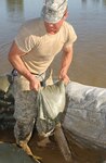 A member of the Iowa National Guard prepares to set a sandbag into place as part of a new 7-foot levee protecting an Ottumwa power sub-station.