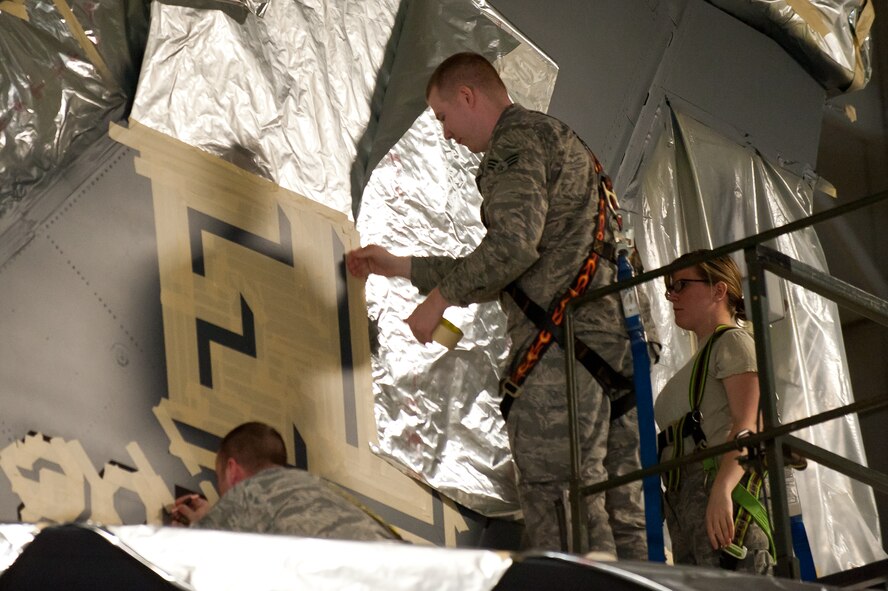 (From left) Staff Sgt. Brian Harrison, Senior Airmen William Moss and Courtney Ramsey, 28th Maintenance Squadron fabrication technicians, tape for shading around letters and numbers while replacing the tail-flash on a B-1 bomber in preparation for an upcoming wing change of command at Ellsworth Air Force Base, S.D., April 2, 2013. A typical Ellsworth B-1 tail flash displays a solid black “EL” and a number, whereas the designated commander B-1s have white shaded areas on the “EL” and number that displays the wing, group or squadron such as “28 BW,” or “34 BS.” (U.S. Air Force photo by Airman 1st Class Kate Thornton-Maurer/Released)