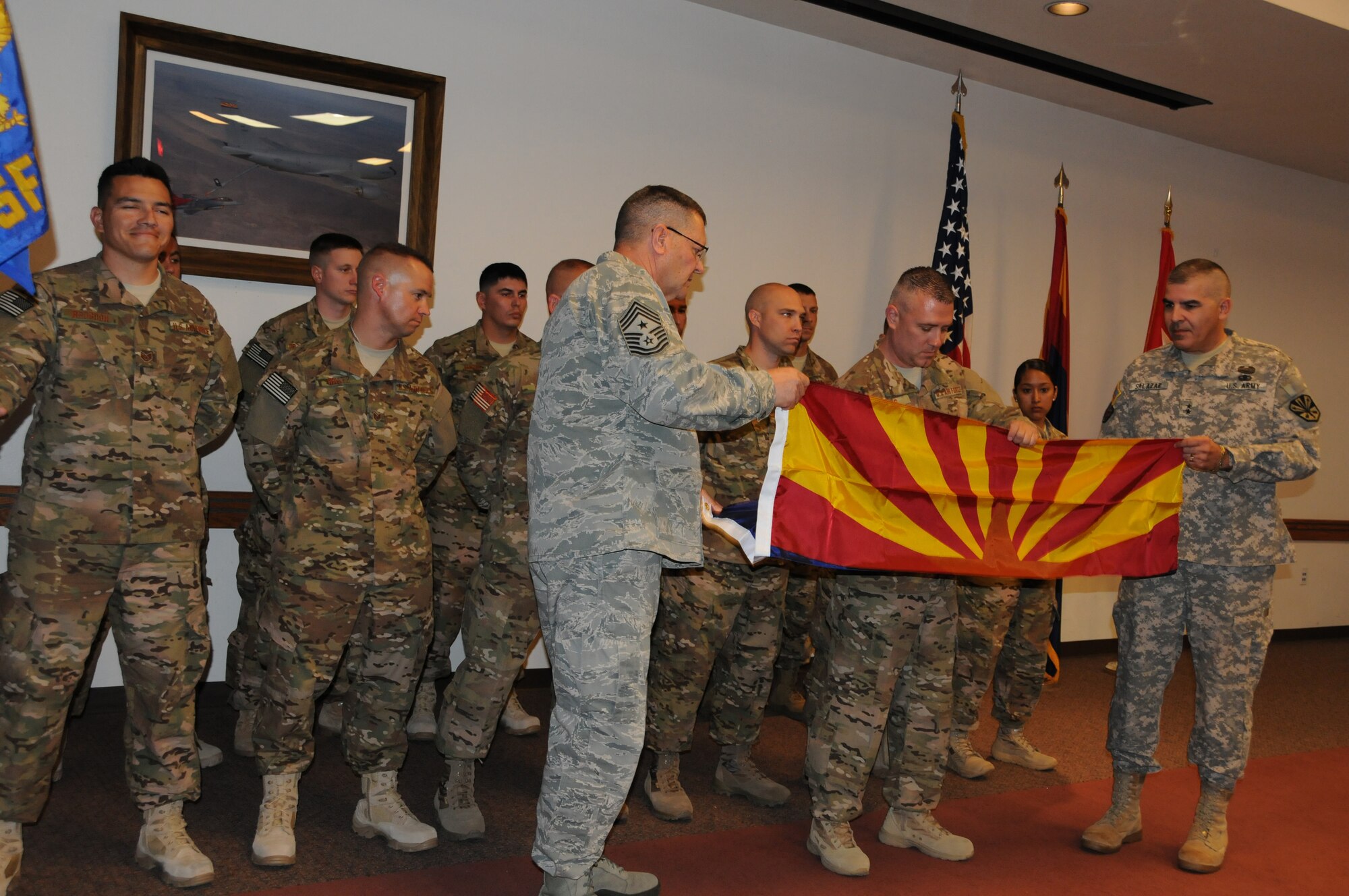 U.S. Air Force Chief Master Sgt. Daniel Irving, Arizona Air National Guard state command chief, presents the Arizona flag to deploying members of the 161st Security Forces Squadron, during a send-off ceremony April 6, 2013. Accepting the flag is U.S. Air Force Master Sgt. Ronald Davis, 161 SFS deployment team leader, with the help of U.S. Army Maj. Gen. Hugo Salazar, Adjutant General, Arizona National Guard. At the ceremony, Chief Irving described the history of the Arizona flag which was designed by Arizona National Guard Col. Charles Wilfred Harris. Colonel Harris was the captain of the unit’s rifle team in 1910 and Arizona was the only team without an emblem. In 1917, the rifle team’s flag became the Arizona State Flag. Chief Irving requested that the team proudly display the Arizona State Flag throughout their deployment. (Air National Guard photo by Tech. Sgt. Susan Gladstein/Released)