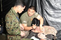 U.S. Navy Petty Officer 2nd Class Fernan P. Diamse, right, demonstrates the lifelike texture of a mannequin’s skin to Japan Ground Self-Defense Force Maj. Gen. Yoshiro Oshika March 28 at the tactical medical simulation center on Camp Hansen. Oshika is the director of the medical department, Ground Staff Office, JGSDF. Diamse is a corpsman with 3rd Medical Battalion, Combat Logistics Regiment 35, 3rd Marine Logistics Group, III MEF.