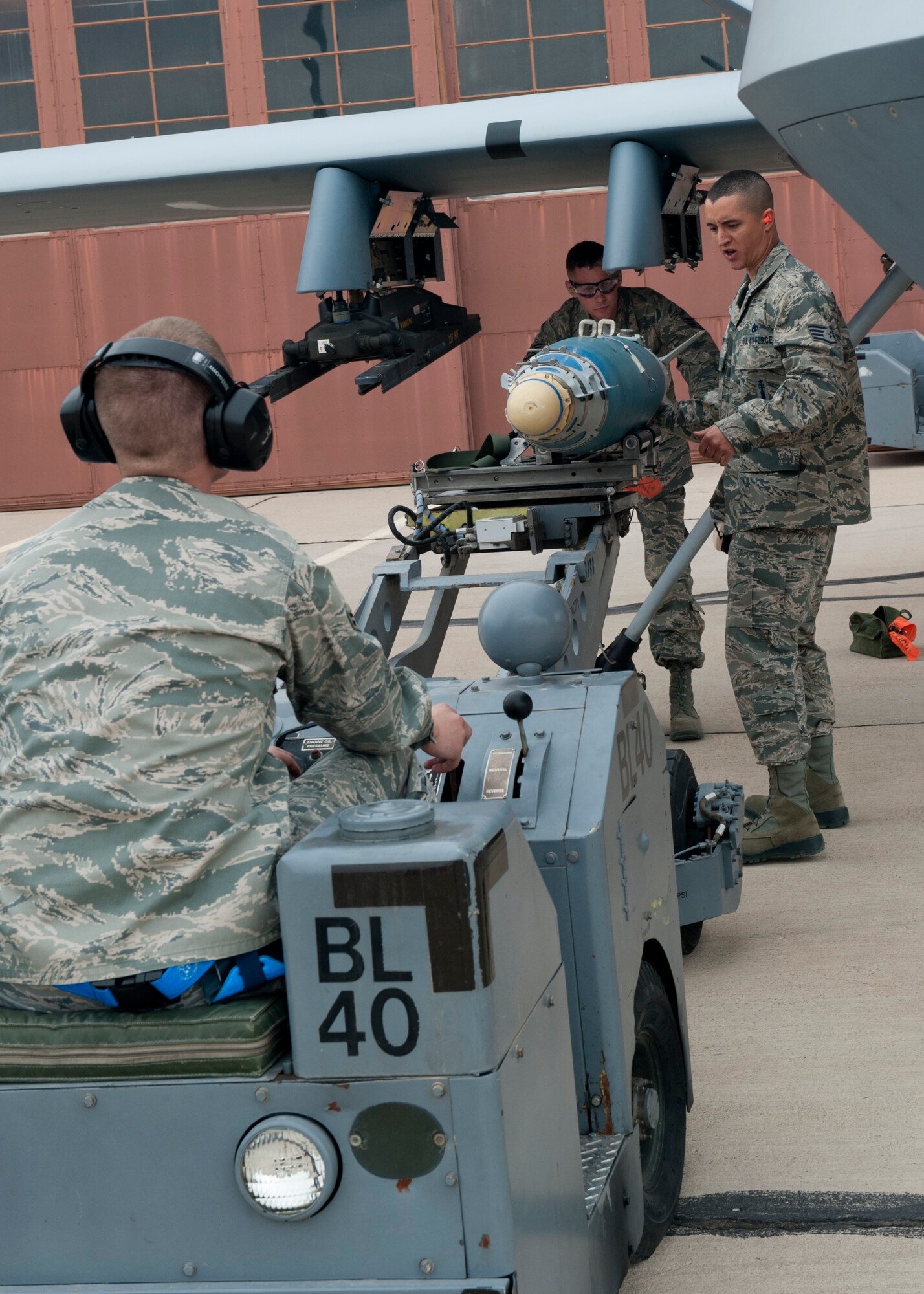 Airman 1st Class Sammy McCain, Staff Sgt. Dustin Ford, and Staff Sgt. Jonathan Adams, all 849th Aircraft Maintenance, load an inert missile onto an MQ-9 Reaper aircraft during a quarterly load-crew competition at Holloman Air Force Base, N.M., April 5. The MQ-9 load-crew competed in the competition to have their skills evaluated alongside the F-22 Raptor aircraft and German Air Force load-crews. For the competition, points are awarded during the weapons-loading, tool kit inspection, and uniform inspection. (U.S. Air Force photo by Airman 1st Class Leah Murray/Released)