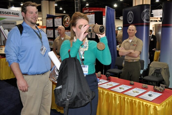 Chief Warrant Officer 2 Joe Davide (right) of Infantry Weapons Systems watches Lindsey Hooyer, a defense contractor from Patuxent River, Md., look through a scope at Marine Corps Systems Command’s exhibit April 8 during the Sea-Air-Space Exposition at the Gaylord National Convention Center in National Harbor, Md.