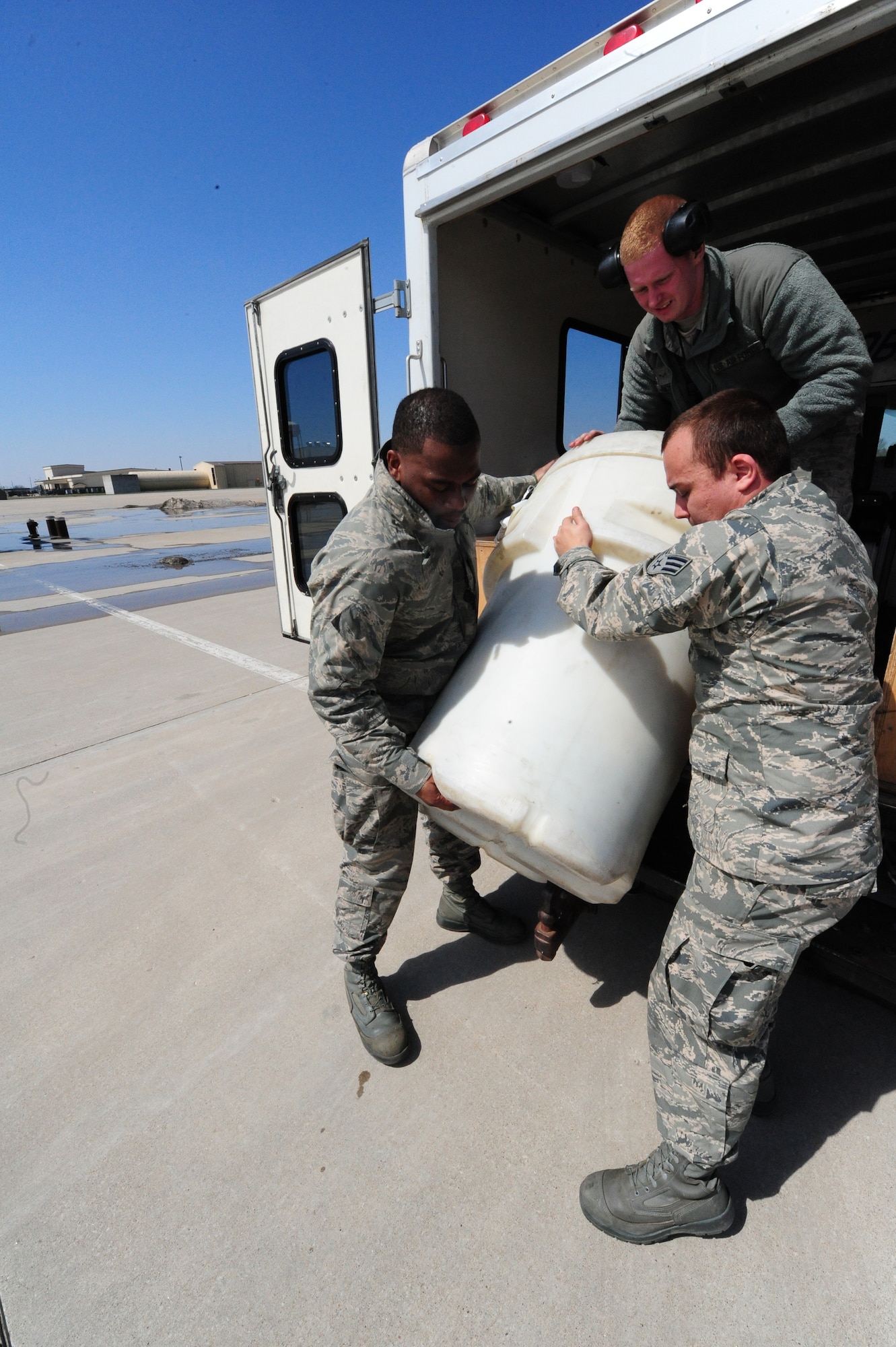 Airmen 1st Class Steven McCray, and James Fulton, 13th Aircraft Maintenance Unit crew chiefs, and Senior Airman Sean Hegstad, 13th AMU crew chief, lift a white barrel spill kit at Whiteman Air Force Base, April 5, 2013. The spill kit was used for an engine-running crew change later that day. (U.S. Air Force photo by Staff Sgt. Nick Wilson/Released)