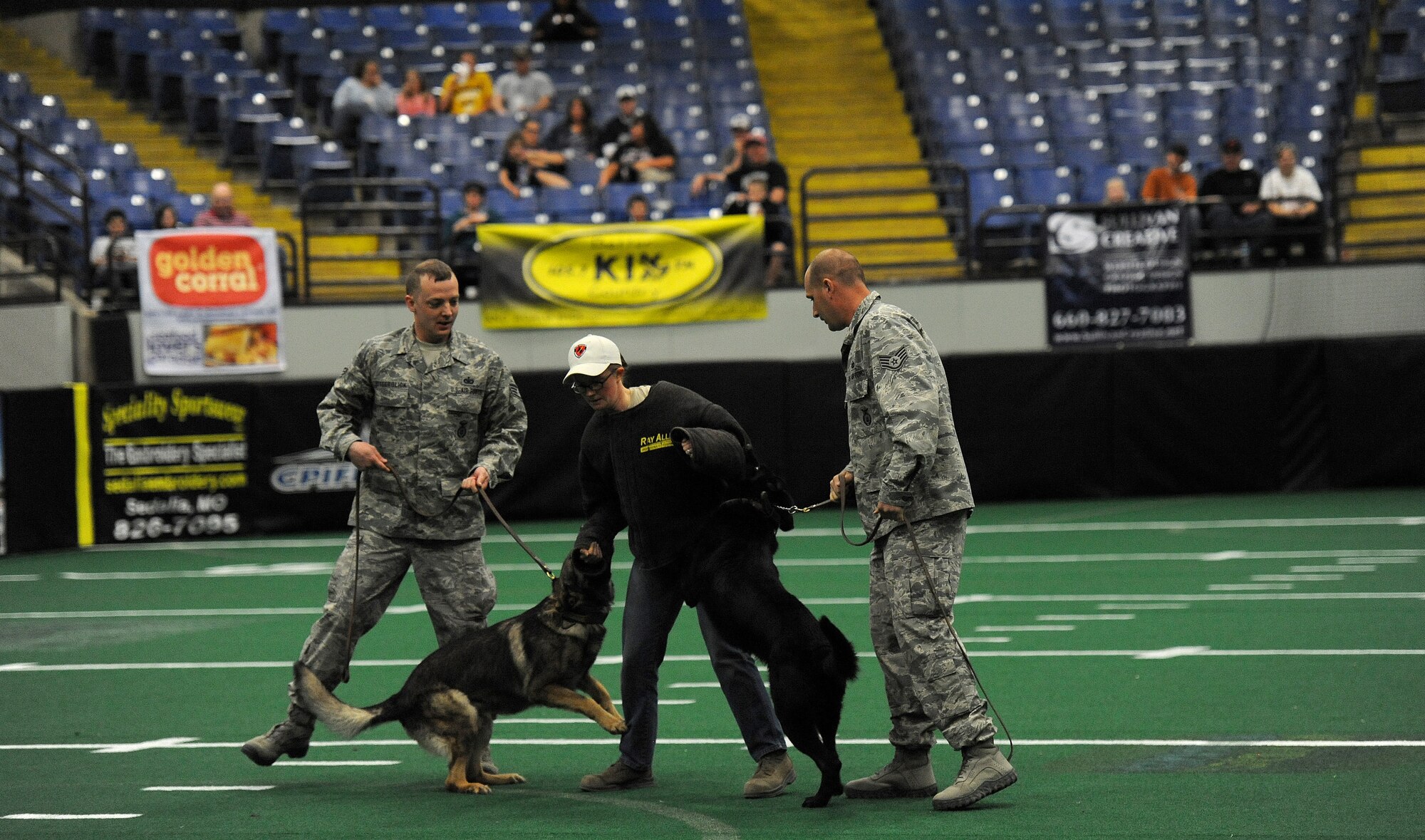Staff Sergeants Jeffrey Besserglick, Amanda Cubbage and Michael Van Deusen, 509th Security Forces Squadron military working dog handlers, provide a military working dog demonstration for a Missouri Outlaw military appreciation game halftime show in Sedalia, Mo., April 6, 2013. The demonstration showed the capabilities of the dogs. (U.S. Air Force photo by Staff Sgt. Nick Wilson/Released)