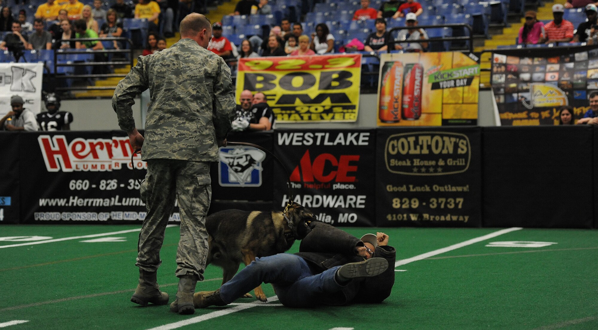 Staff Sgt. Michael Van Deusen, 509th Security Forces Squadron military working dog handler, supervises as Staff Sgt. Amanda Cubbage, 509th SFS military working dog handler, acts as an aggressor during a demonstration for a Missouri Outlaw military appreciation game in Sedalia, Mo., April 6, 2013. Military working dogs are trained to bite into a suspect and hold on until the handler can take control. (U.S. Air Force photo by Staff Sgt. Nick Wilson/Released)
