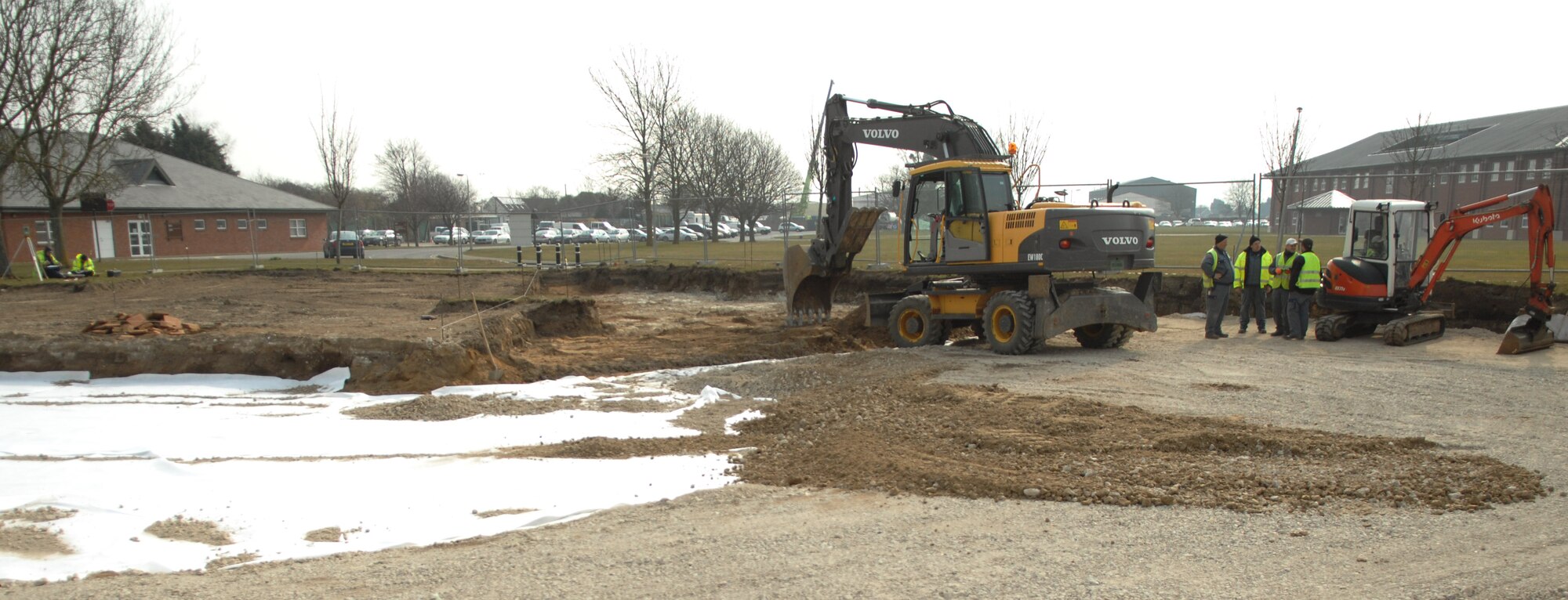 Construction workers from the 38th Construction Training Squadron, Ramstein Air Base, Germany, speak to each other after spreading dirt and gravel in a parking lot construction site April 9, 2013, behind building 591 on RAF Mildenhall, England. The parking lot will be used to accommodate parking for the 100th Communications Squadron members slated to move into building 591. The building the 100th CS is currently in will be demolished to make way for a road. (U.S. Air Force photo by Airman 1st Class Dillon Johnston/Released)