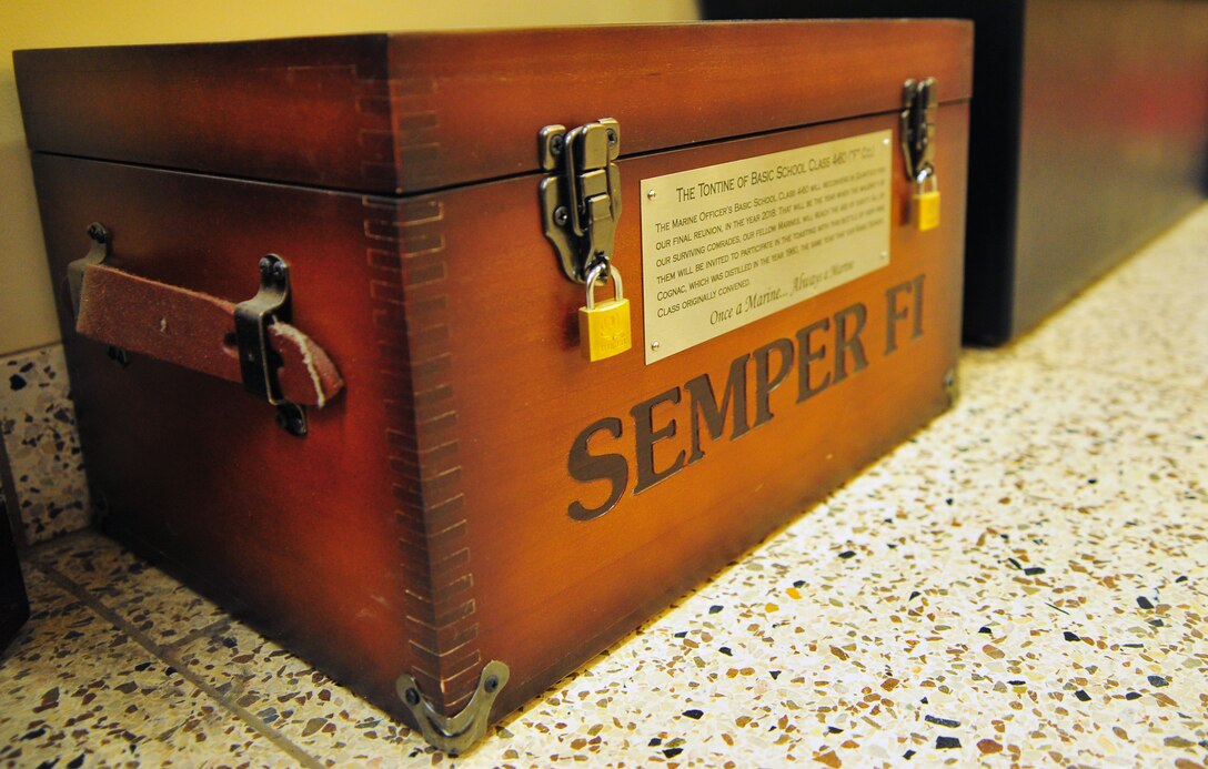 Between a tall glass case filled with engraved chrome and crystal plaques, and another case holding a stoic bronze statue of Chesty Puller leading a charge - sits a double padlocked wooden box emblazoned with the Marine Corps emblem.