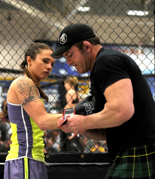 Coach Matt Powers, helps his kickboxer, Elisha Helsper, put her gloves on before entering the octagon to face fellow kickboxer, Aerial Beck, during the second of six fights at 221 Industries’ first-ever Fight For the Troops event at Malmstrom Air Force Base, Mont., on April 5. Beck won the matchup by split decision. (U.S. Air Force photo/Staff Sgt. R.J. Biermann)