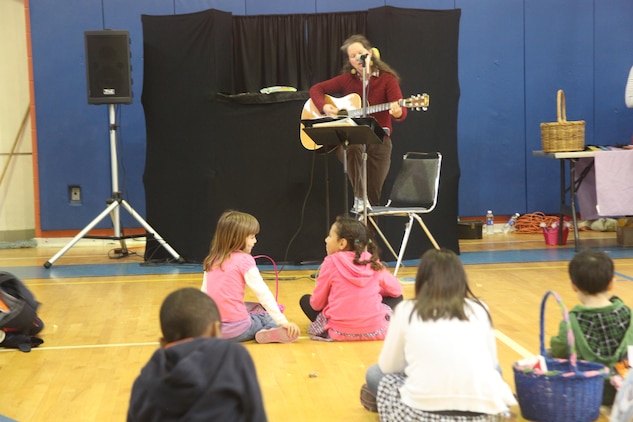 Children gather around as Cmdr. Kim Donahue, the MAG 31 chaplain, plays guitar and sings for families during Eggstravaganza, March 23. After rain sent everyone indoors many found the gymnasium a great place to relax and spend time with family and friends between activities. 