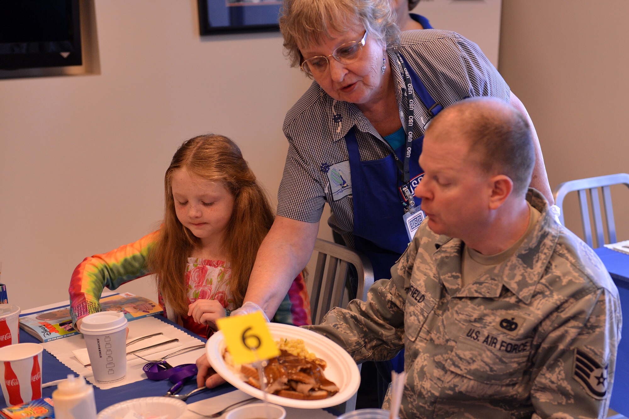 USO volunteer Jean Pescar serves dinner to Staff Sgt. Bradley Burfield, 62nd Aerial Port Squadron cargo processing supervisor, and his daughter Kayli, during the USO's “No Dough Dinner” night, April 11, 2013, at Joint Base Lewis-McChord, Wash. The USO's new no program Airmen and their families a free dinner one night toward the end of each pay period. (U.S. Air Force photo/Airman 1st Class Jacob Jimenez)
