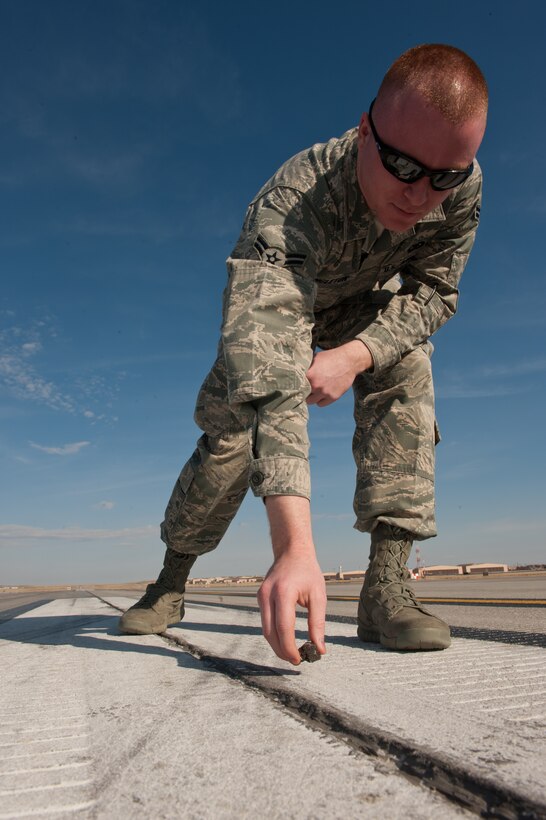 Airman 1st Class Steven Singleton, 28th Operation Support Squadron airfield management specialist, picks up a rock during a foreign object and debris check on the active runway on Ellsworth Air Force Base, S.D., April 4, 2013. Priced at more than $3,700,000 each, a B-1 bomber’s engines and a variety of other vital parts – flight controls, ejection seats and cockpit controls – can easily become inoperative if a foreign object finds its way into the wrong place. (U.S. Air Force photo by Airman 1st Class Kate Thornton-Maurer/Released)  