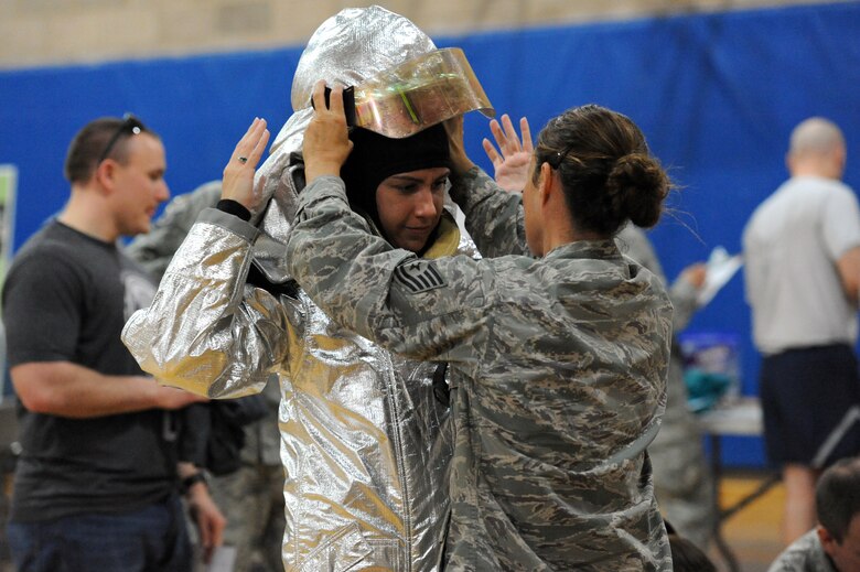 Capt. Katherine Danos, 386th Expeditionary Medical Group is aided by Tech. Sgt. Andrea Murdaugh, 386th Expeditionary Civil Engineering Squadron firefighter with the donning of the fire suit during the 386th Air Expeditionary Wing wellness fair Apr 13, 2013. The wellness fair was represented by more than 20 wing agencies which provided information and resources to the service members and civilians assigned to ‘The Rock’. (U.S. Air Force photo by Senior Master Sgt. George Thompson)