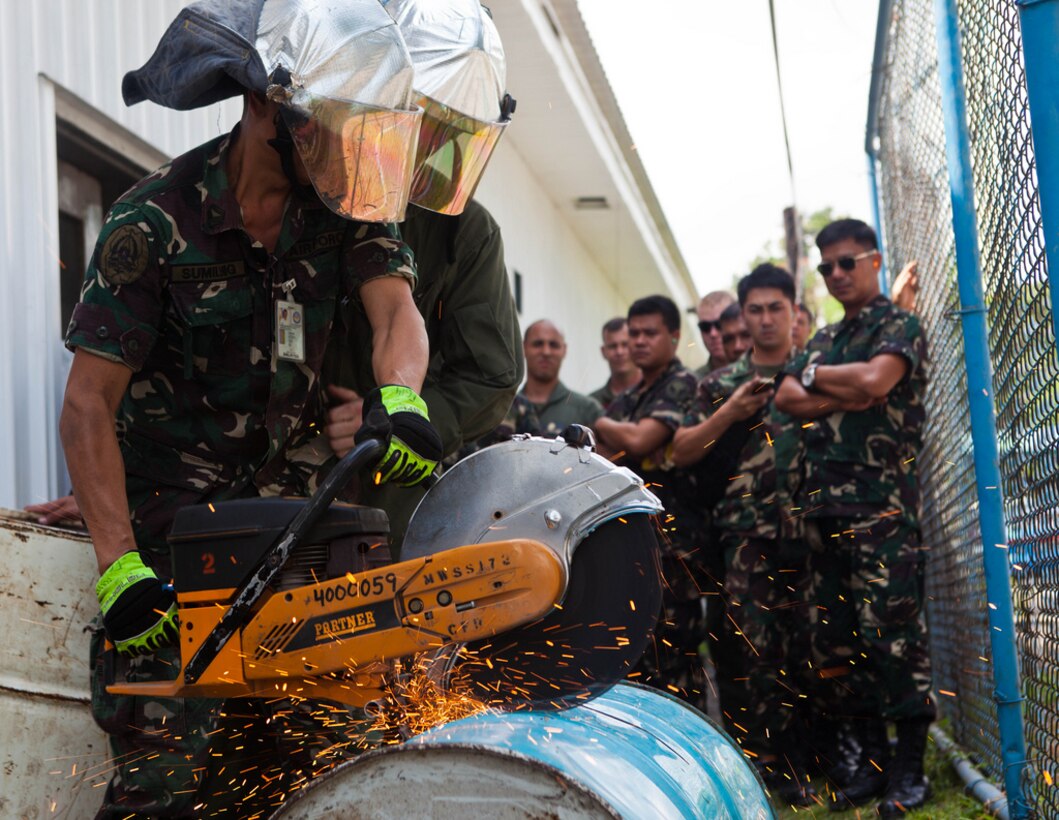 U.S. Marine Lance Cpl. Justin D. Groom, second from left, braces Philippine Air Force Technical Sgt. Arthuro Sumilhig as he cuts into a barrel with a K-12 rescue saw April 8 at Clark Field, Philippines. Filipino and U.S. firefighters exchanged tactics and techniques to better prepare themselves for future emergencies. The training was part of exercise Balikatan 2013, an annual bilateral training evolution aimed at ensuring interoperability of the Philippine and U.S. militaries during planning, contingency and humanitarian assistance operations.