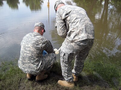 Sgt. Keith Yohnke (left) and Staff Sgt. Steve Brouillet from the Iowa National Guard's 71st Weapons of Mass Destruction-Civil Support Team take a water sample for analysis June 19 from a flooded area near Manchester, Iowa, to assist state and federal authorities and identify hazardous materials released in the Midwest floods.