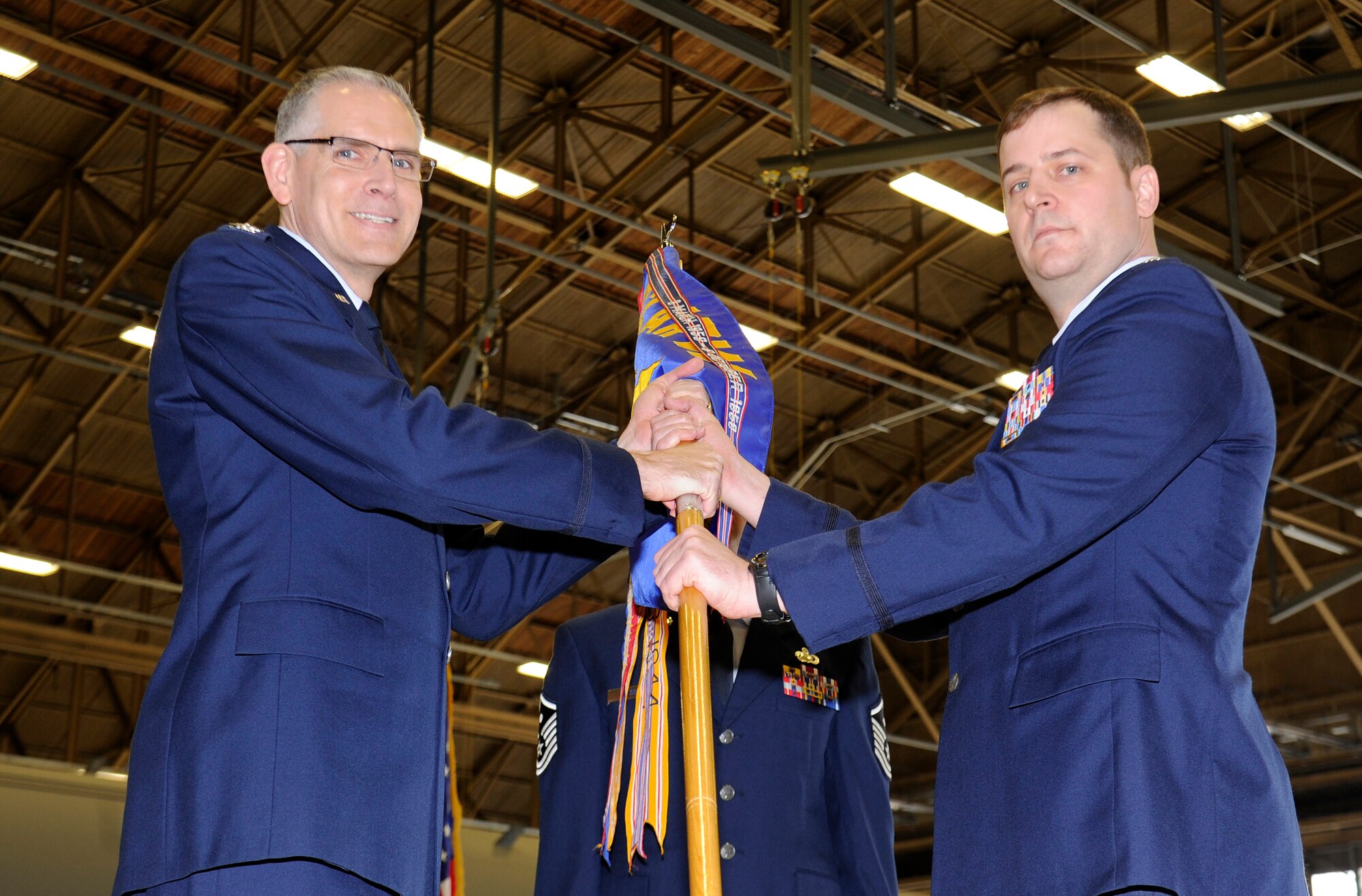 Col. Shawn Teagan, 92nd Operations Group commander, hands off the guidon to Lt. Col. Timothy Danielson, 92nd Operations Support Squadron commander during the 92nd OSS change of command ceremony inside hangar 2 at Fairchild Air Force Base, Wash., April 12, 2013. The change of command ceremony is a tradition that represents a formal transfer of authority and responsibility. (U.S. Air Force photo by Airman 1st Class Ryan Zeski)