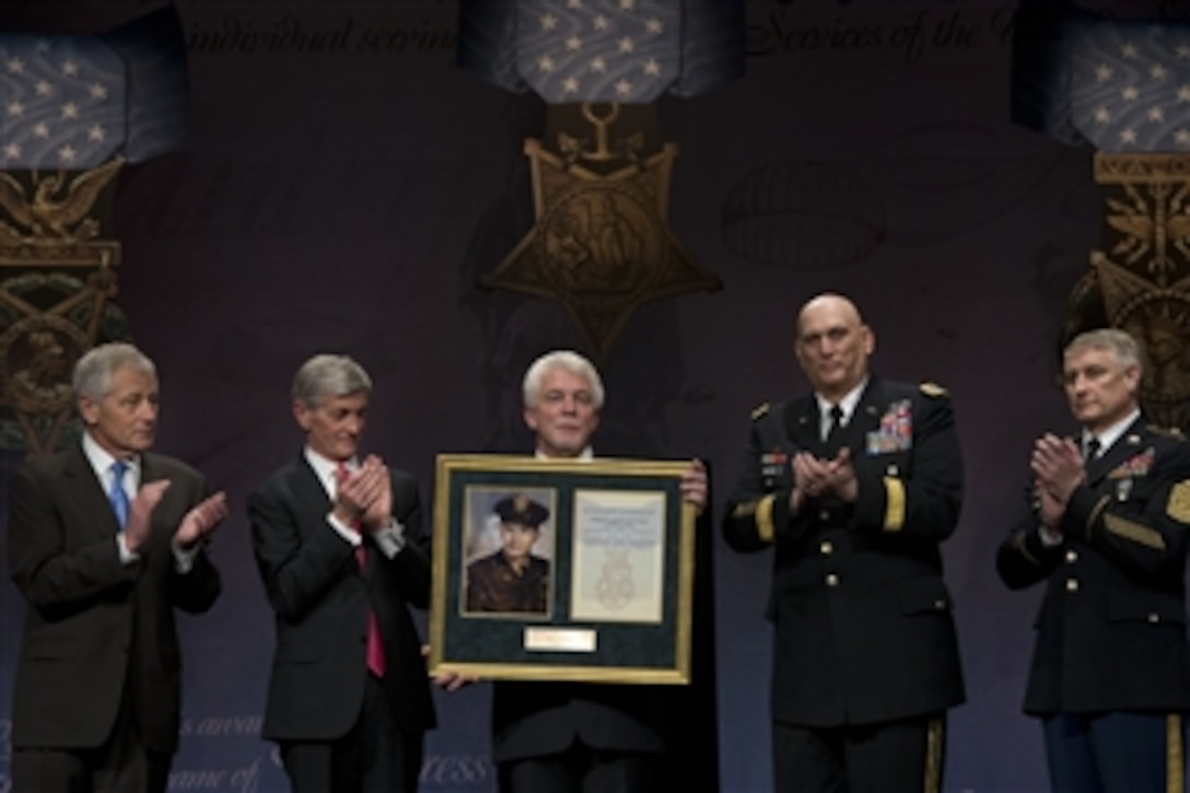 Secretary of Defense Chuck Hagel, left, Secretary of the Army John McHugh, second from left, Chief of staff of the Army Gen. Raymond Odierno, second from right, and Sgt. Maj. of the Army Raymond Chandler III, right, applaud as Ray Kapaun holds a framed photo of his uncle Medal of Honor recipient Army Chaplain (Capt.) Emil J. Kapaun at a Hall of Heroes induction ceremony on April 12, 2013.  Chaplain Kapaun died in a prisoner of war camp during the Korean War while counseling and saving countless fellow service members.  