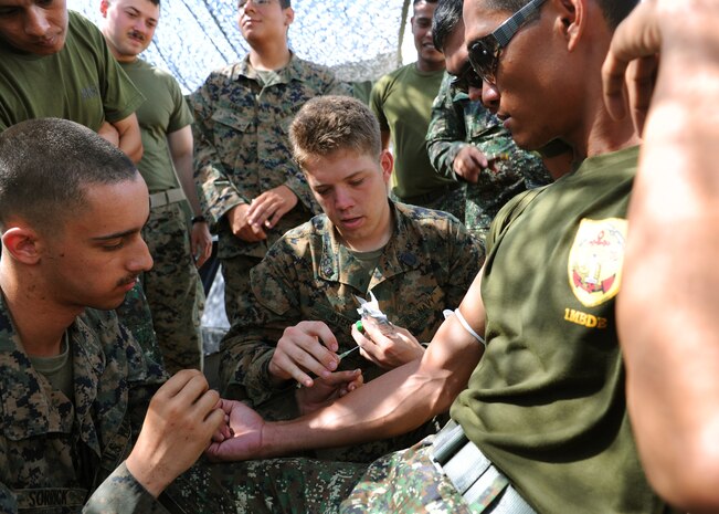 From left to right: U.S. Marine Lance Cpl. Andrew Sorrick, small arms repair technician and Mill City, native, with 3rd Ordinance Maintenance Company, Combat Logistics Regiment 35, 3rd Marine Division, III Marine Expeditionary Force, observes U.S. Navy Austin Byers, Gilbert, Ariz., native, and corpsman combat life saver instructor with the 3rd Medical Battalion, Combat Logistics Regiment 35, 3rd Marine Logistics Group, III Marine Expeditionary Force, demonstrate an intravenous injection on Philippine Marine Private 1st Class Rixson Romo, a Zamboanga City native and driver with the Marine Transportation and Maintenance Battalion during a combat life saver course at Camp O' Donnell April 13. The combat life saver training was part of Balikatan 2013, an annual bilateral training exercise in its 29th iteration designed to enhance interoperability between both forces and strengthen military-to-military relations.
