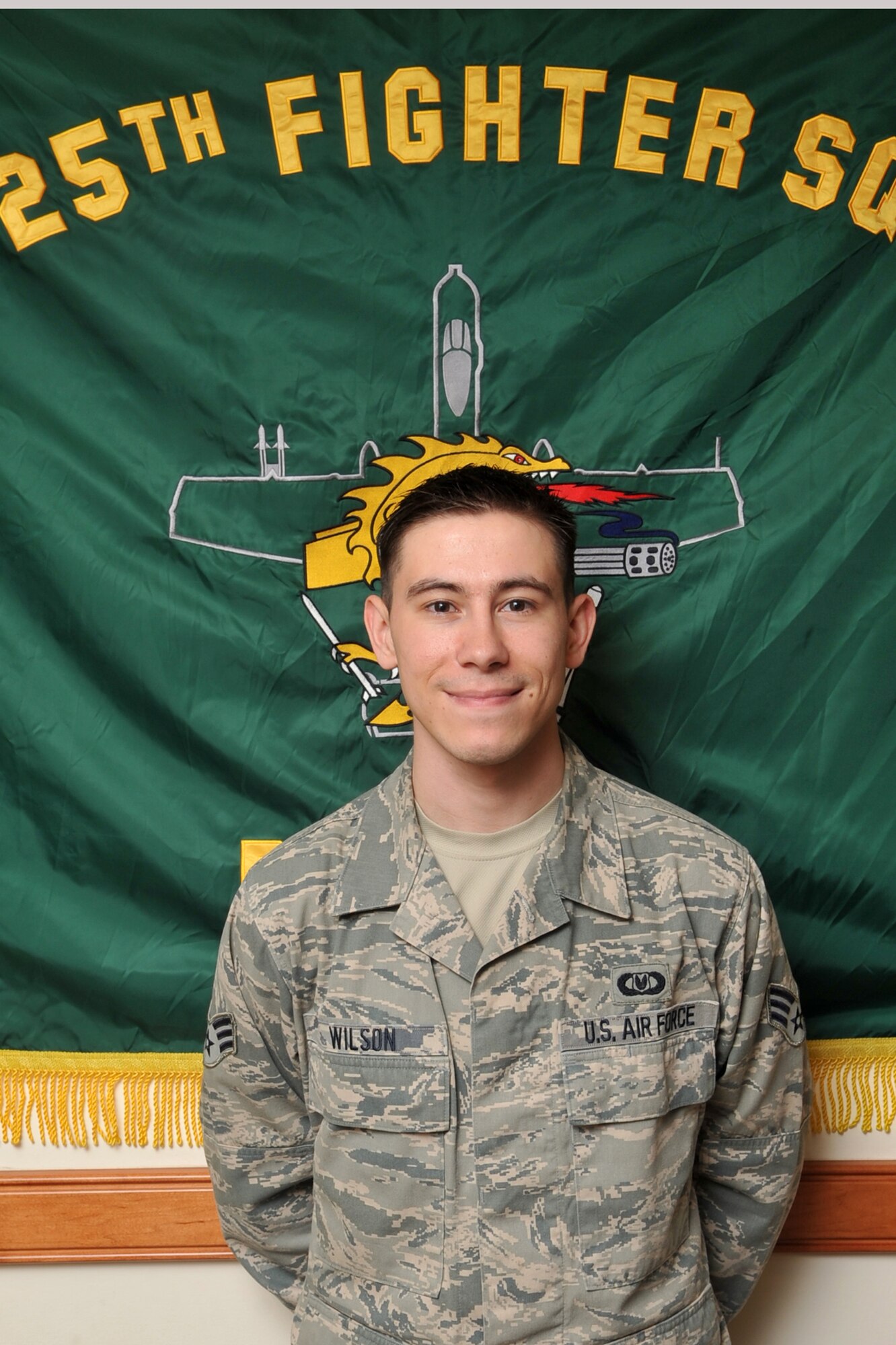 Senior Airman Charles Wilson, 51st Operations Support Squadron aircrew flight equipment technician who works with the 25th Fighter Squadron, stands in front of the 25th FS's flag to be recognized as the Airman Spotlight at Osan Air Base, Republic of Korea, April 16, 2013.  (U.S. Air Force photo/Tech Sgt. Raymond Mills)