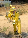 Sgt. Mark Walch from Company A, 297th Support Battalion, one of the initial 295 Soldiers mobilized to fight the wildfires burning in California, uses an ax to cut down trees to form a fire break preventing burning material from crossing lines and spreading to unburned areas. Walch, a high school teacher from Chico, Calif., volunteered immediately to be part of the first Soldiers to fight fires on the ground in California in 30 years.