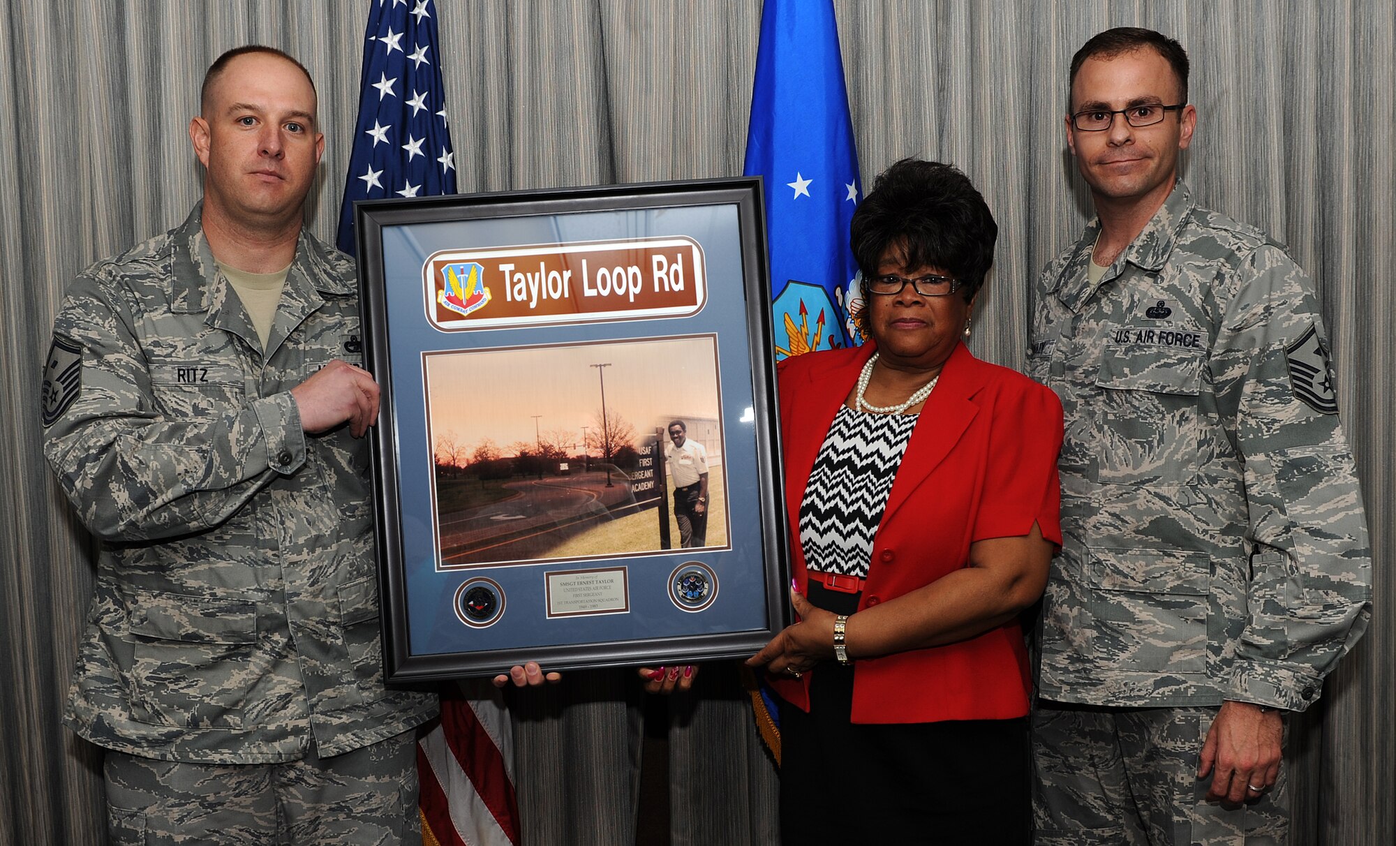 U.S. Air Force Master Sgts. John Ritz and Ryan McCauley present a gift to Mary Taylor, widow of Senior Master Sgt. Ernest Taylor during a dedication ceremony for Taylor Loop Road at Langley Air Force Base Va., April 12, 2013. Taylor was a first sergeant for what used to be the 1st Transportation Squadron until his untimely death in 1983. (U.S. Air Force photo by Senior Airman Teresa Aber/Released)
