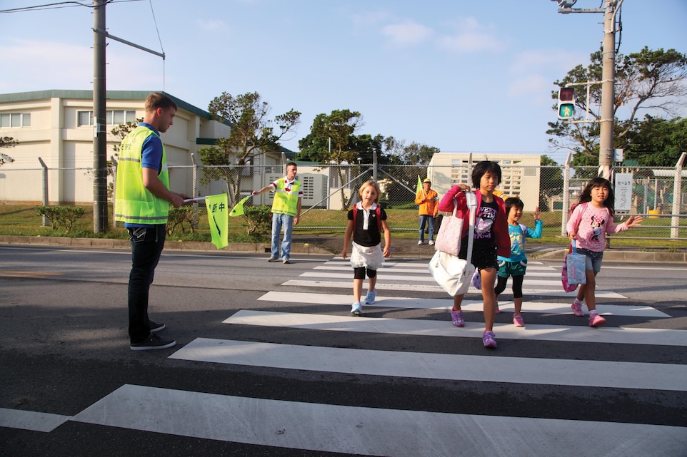 Lance Cpls. Josiah A. LeCleir, front, and Tyler D. Baldwin help children safely cross the road on their way to school April 15 in Uruma City. As part of a two-week safety campaign, Marines volunteered to help new students learn proper procedures for safely crossing roads. LeCleir is a ground radio operator with Headquarters Battalion, 3rd Marine Division, III Marine Expeditionary Force, and Baldwin is a telephone systems and personal computer repairer with the battalion.