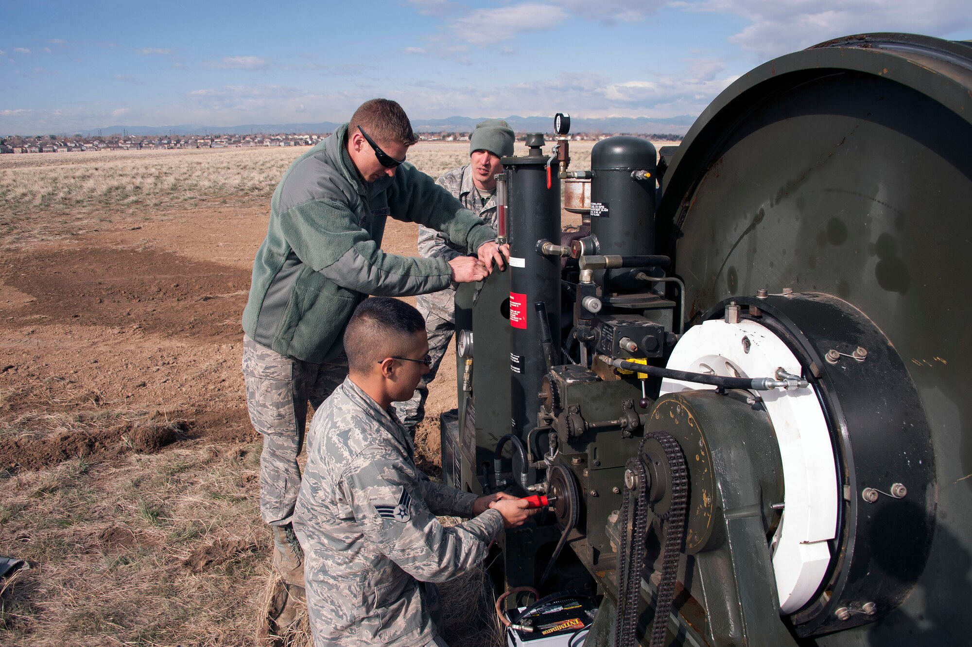 Civil Engineers and a Red Horse Unit are working together to install a BAK-12, Expeditionary Aircraft Arresting System on the main runway at Buckley Air Force Base.  The temporary system must be installed prior to any construction taking place on the runway and so the permanent arresting systems can be upgraded. Senior Airman Jesus Martinez (near) from the 460th Space Warning Squadron, Staff Sgt. Alex Atkins (center) from the 140th Wing and Staff Sgt. Issac Strickler from the 200th Red Horse unit adjust the braking system of the BAK-12 Aircraft Arresting system as part of the installation process.  (U.S. Air National Guard photo by Senior Master Sgt. John Rohrer)
