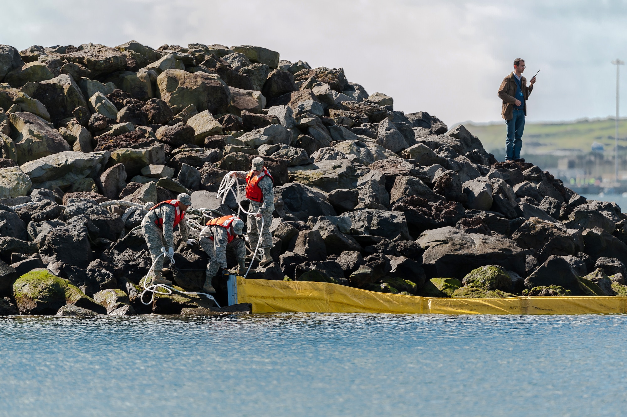 (l-r) Tech Sgt. Tony Andres, Staff Sgts. Angel Diaz-Berrios and Matthew Weffer, all 65th Civil Engineer Squadron water and fuel system maintenance, secure a spill containment boom to the marina breakwater under the supervision of Vitor Berbereia 65th Civil Engineer Squadron Environmental engineer and Spill Prevention and Response Program manager April 18, 2013, Praia da Vitoria, Azores.  These engineers are responding to a simulated fuel spill during an exercise at the Praia fuel bay. (Photo by Lucas Silva/released) 