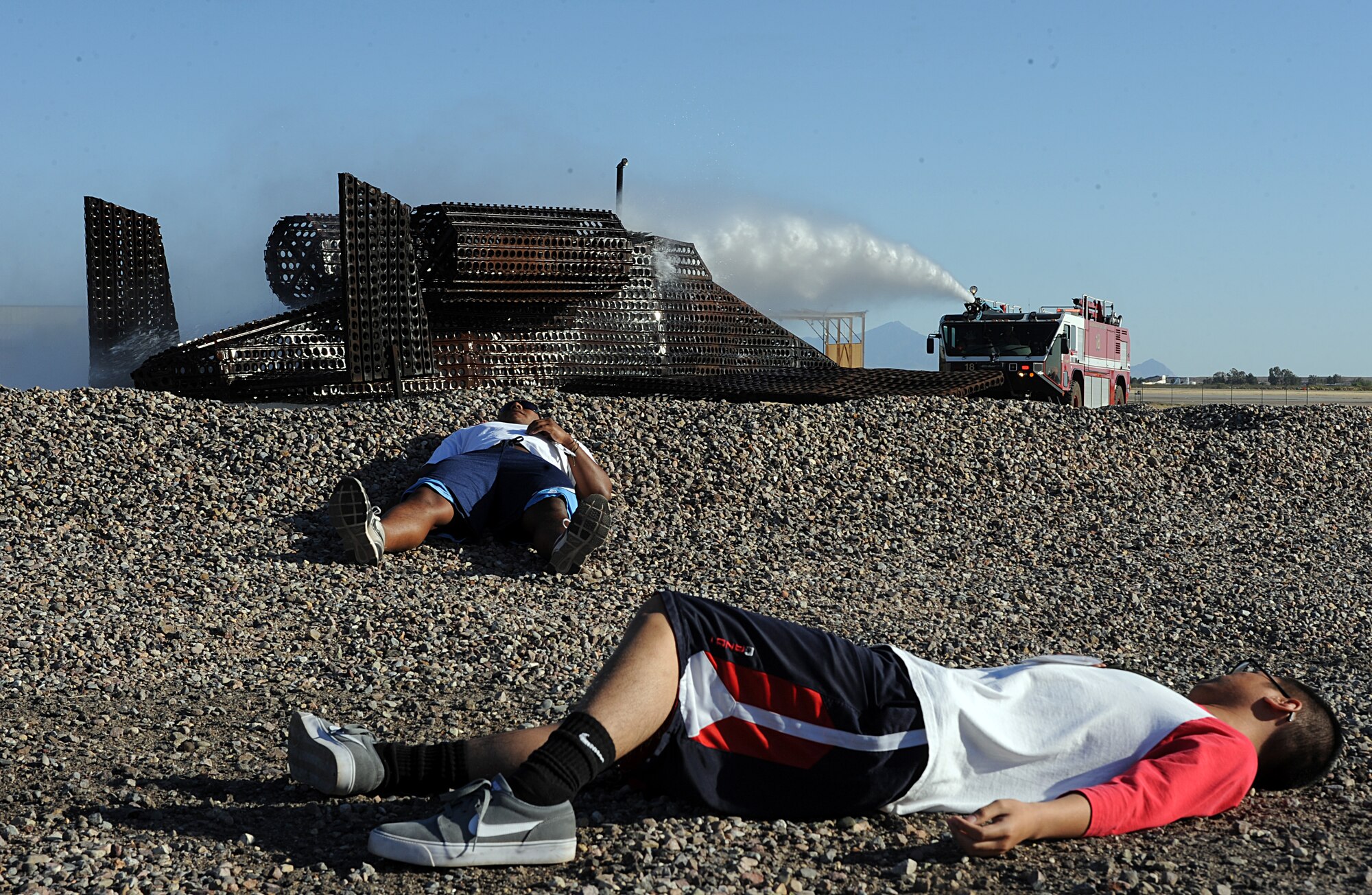 U.S.  Air Force Airman 1st Class Daniel Dulay (foreground) and Senior Airman Sammie Ervan, both from the 355th Logistics Readiness Squadron, lay on the ground as victims of a simulated aircraft crash while firefighters from the 355th Civil Engineer Squadron douse the simulated crashed aircraft during Angel Thunder at Davis-Monthan Air Force Base, Ariz., April 13, 2013. The Angel Thunder exercise grants rescue teams the opportunity to train in a realistic environment. (U.S. Air Force photo by Senior Airman Timothy Moore/Released)