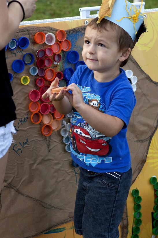 MARINE CORPS BASE HAWAII - A young boy holding a bottle cap extends his arm out to receive a drop of glue from one of the volunteers so he can glue it to the artwork during an event near Riseley Field at Marine Corps Base Hawaii, April 16, 2013. This was one of the events held during “Eco-Friendly In the Park,” which gave children an opportunity to create arts and crafts out of recyclables. (U.S. Marine Corps photo by Lance Cpl. Matthew Bragg)