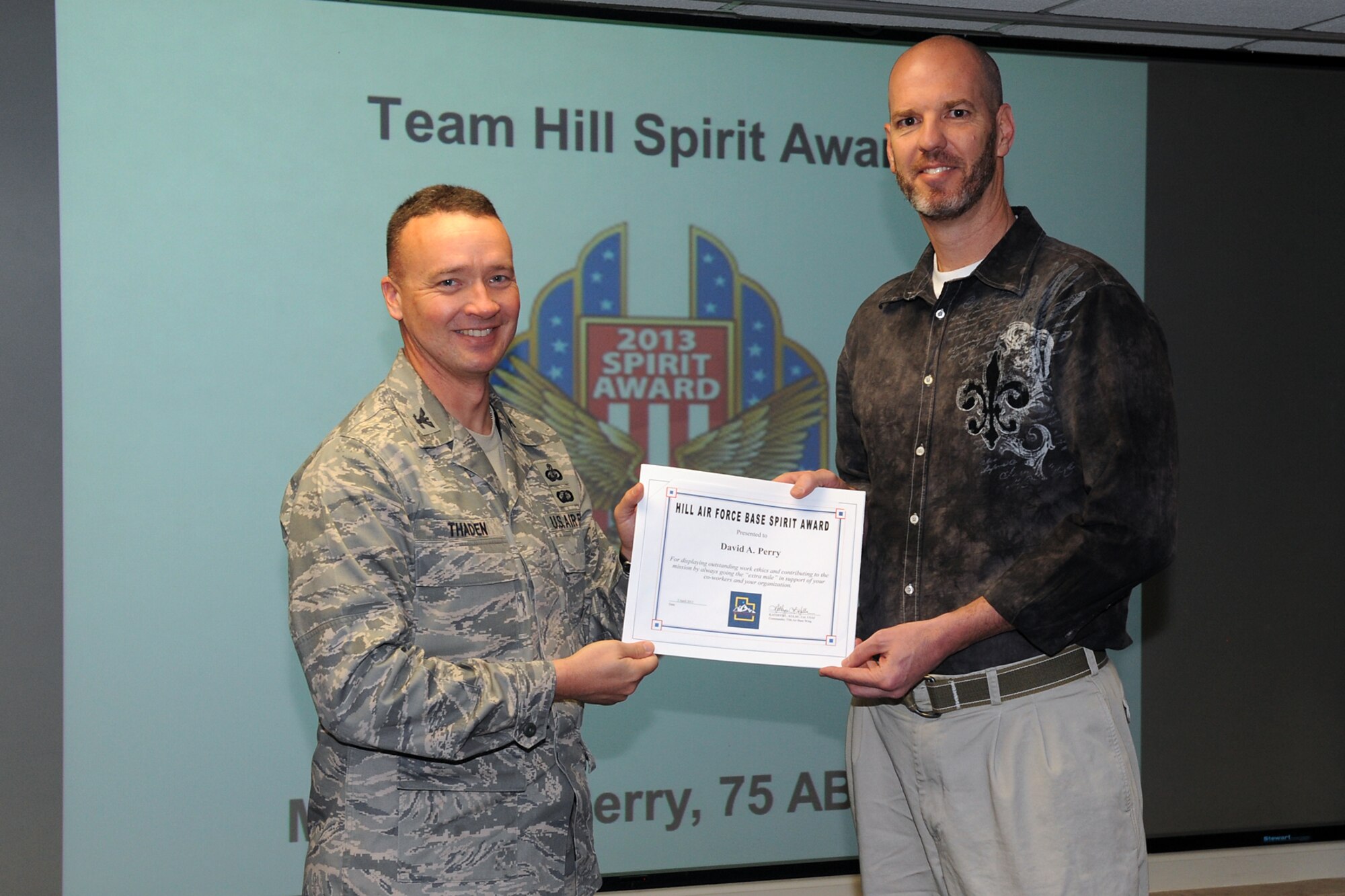 Col. Frederick Thaden, 75th Air Base Wing vice commander, presents David Perry, 75th ABW graphic designer, with a certificate announcing his winning design for the Team Hill Spirit Pin, on April 5. (U.S. Air Force photo/Alex R. Lloyd)