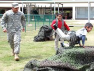 Spc. Sammy Rosado of the 470th Military Intelligence Brigade supervises two Bowden Elementary School students as they master an obstacle course during their field day April 5.  Photo by Gregory Ripps