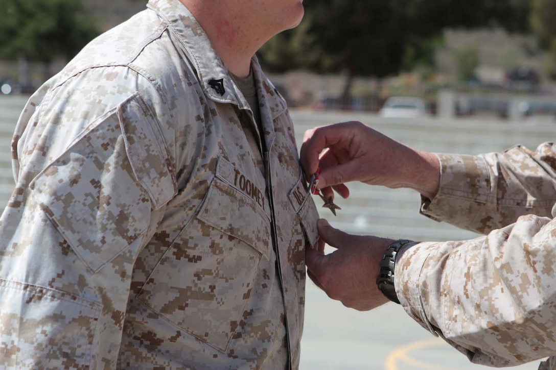 Corporal Michael P. Toomey, a rifleman serving with 2nd Battalion, 5th Marine Regiment, receives the Bronze Star Medal with a Combat V during a ceremony here, April 18, 2013. Toomey, a native of San Francisco, was recognized for his heroic actions on May 8, 2012, while deployed to Musa Qal'ah district, Helmand province, Afghanistan. He led a fire team of Marines in a hasty ambush against an insurgent machine gun team hiding in a tree line. During the assault, Toomey shot an enemy fighter and threw a grenade at their position, causing the remaining insurgents to flee and abandon fighting the Marines for the remainder of the operation.