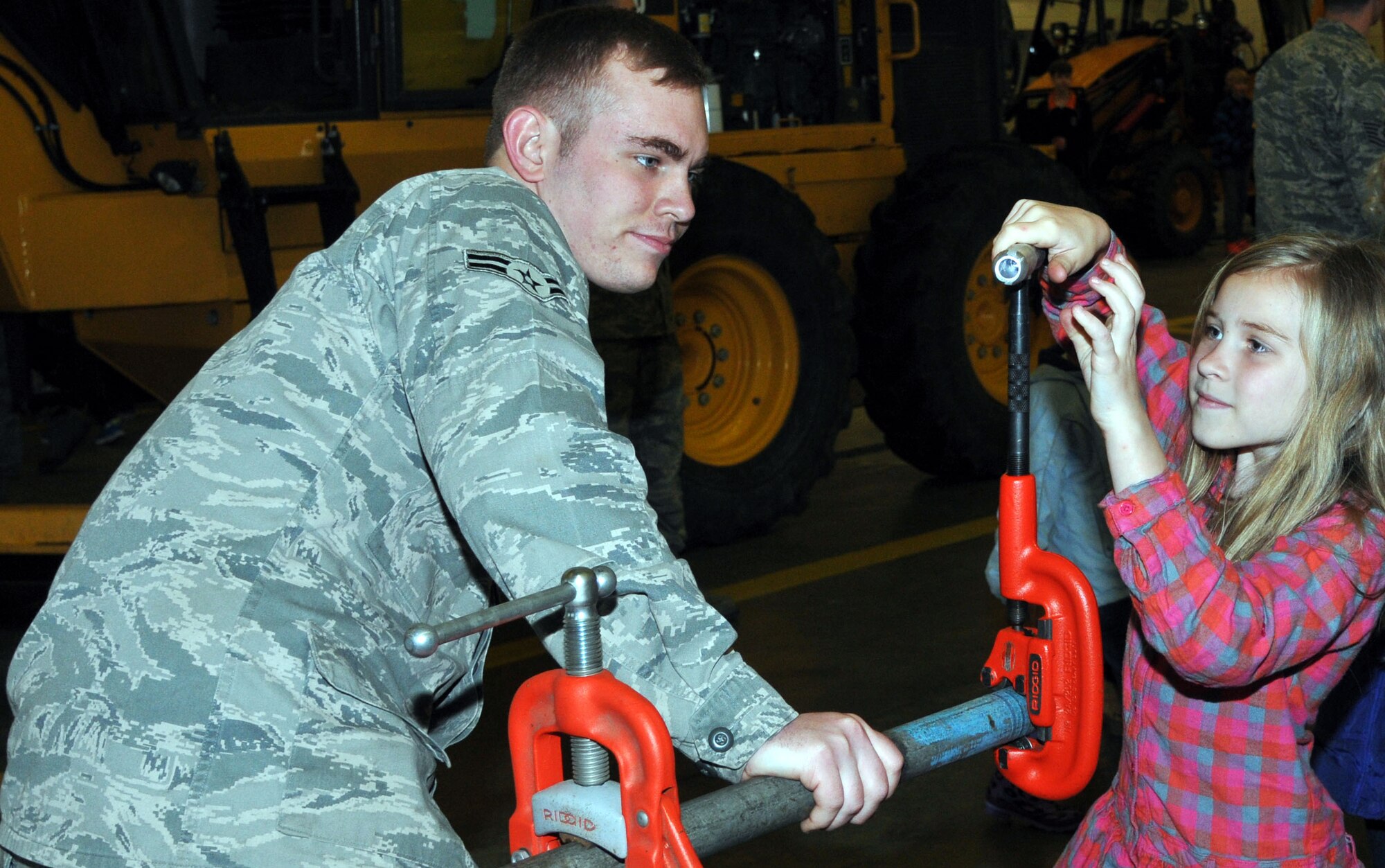 Airman 1st Class Ian Adams, 100th Civil Engineer Squadron Water and Fuels Systems apprentice from Farmers Branch, Texas, supervises Kara Krogmann, 8, daughter of Tech. Sgt. Heath Krogmann, 100th Logistics Readiness Squadron Fixed Facility supervisor,  as she cuts a piece of pipe at a 100th CES static display April 19, 2013, at RAF Mildenhall, England. Job Shadow Day was for k-12 students and was a joint effort between the Department of Defense Schools, RAF Lakenheath and RAF Mildenhall. (U.S. Air Force photo by Airman 1st Class Kelsey Waters/Released)