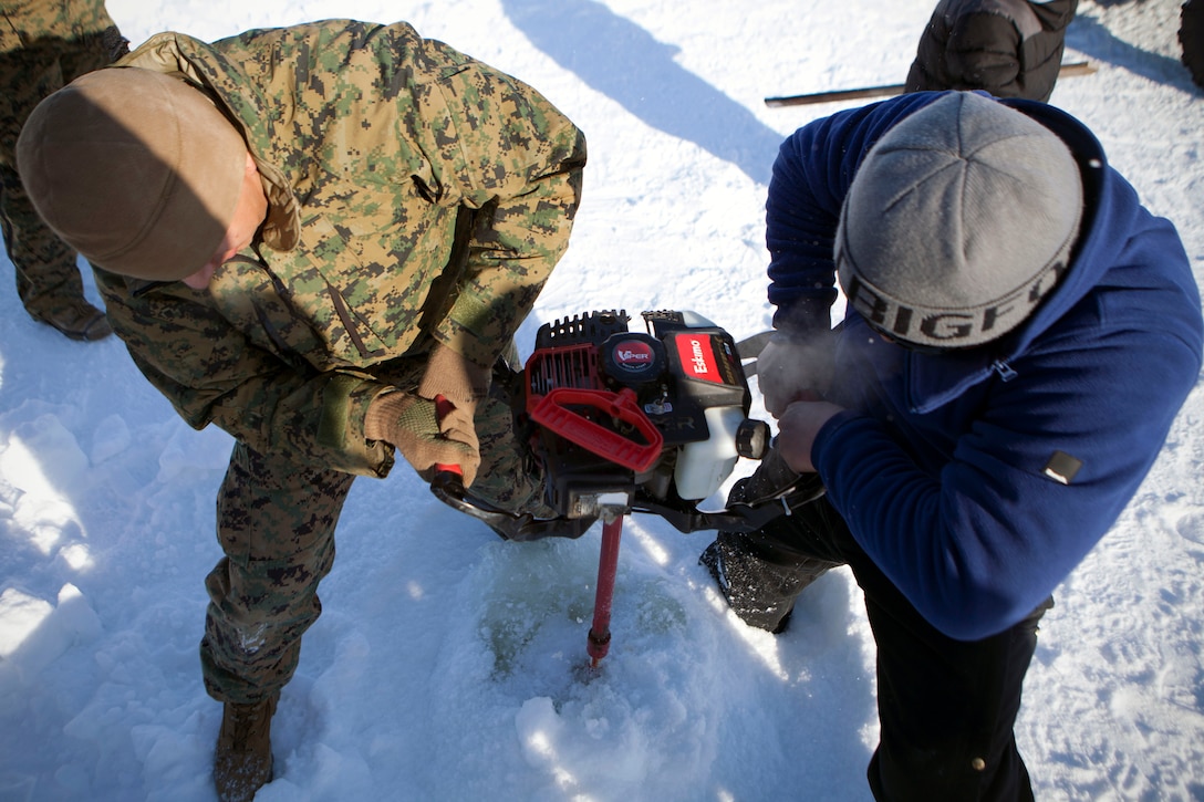 Cpl. Gabriel Castroena, an electrician with 4th Medical Battalion, 4th Marine Logistics Group, Marine Forces Reserve, and a native of San Bernardino, Calif., helps Jung In, a local fishing enthusiast, dig a hole in ice with an auger on the outskirts of Kotzebue, Alaska, April. 17. In, who invited the Marines to ice fish, said they were really eager to help and handled the machine really well. 