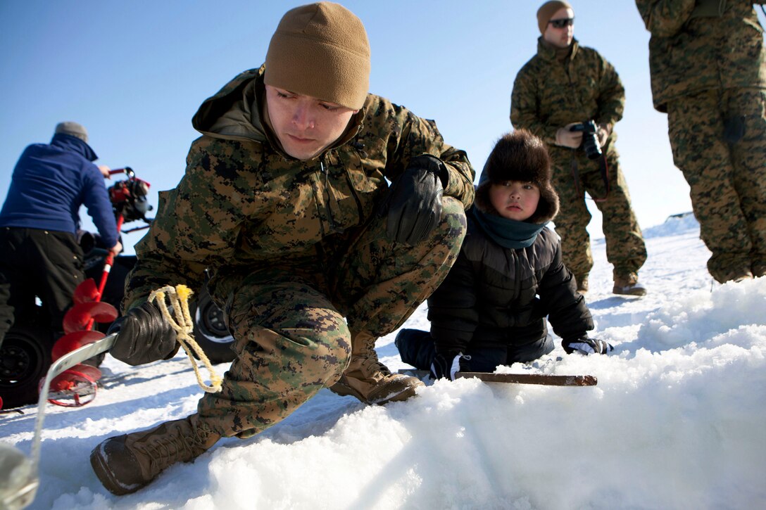 Cpl. Jesus Godiez of 4th Medical Battalion, 4th Marine Logistics Group, Marine Forces Reserve, helps a local child empty an ice hole he helped dig  April 17. Godiez and other service members participating in Innovative Readiness Training Arctic Care 2013 were invited to ice fish after working hours. 